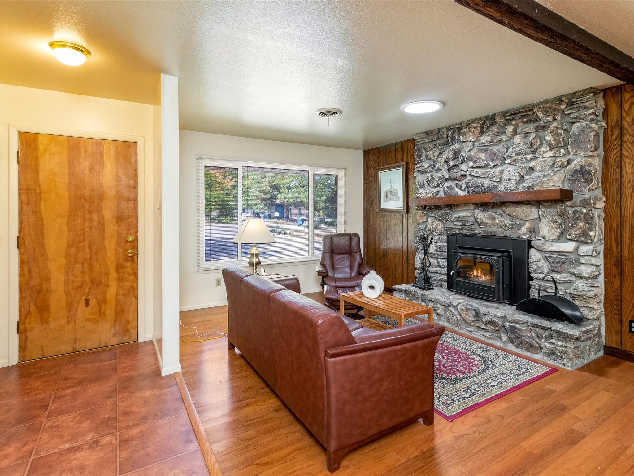 Living room with a stone fireplace, leather seating, and a tiled entry.