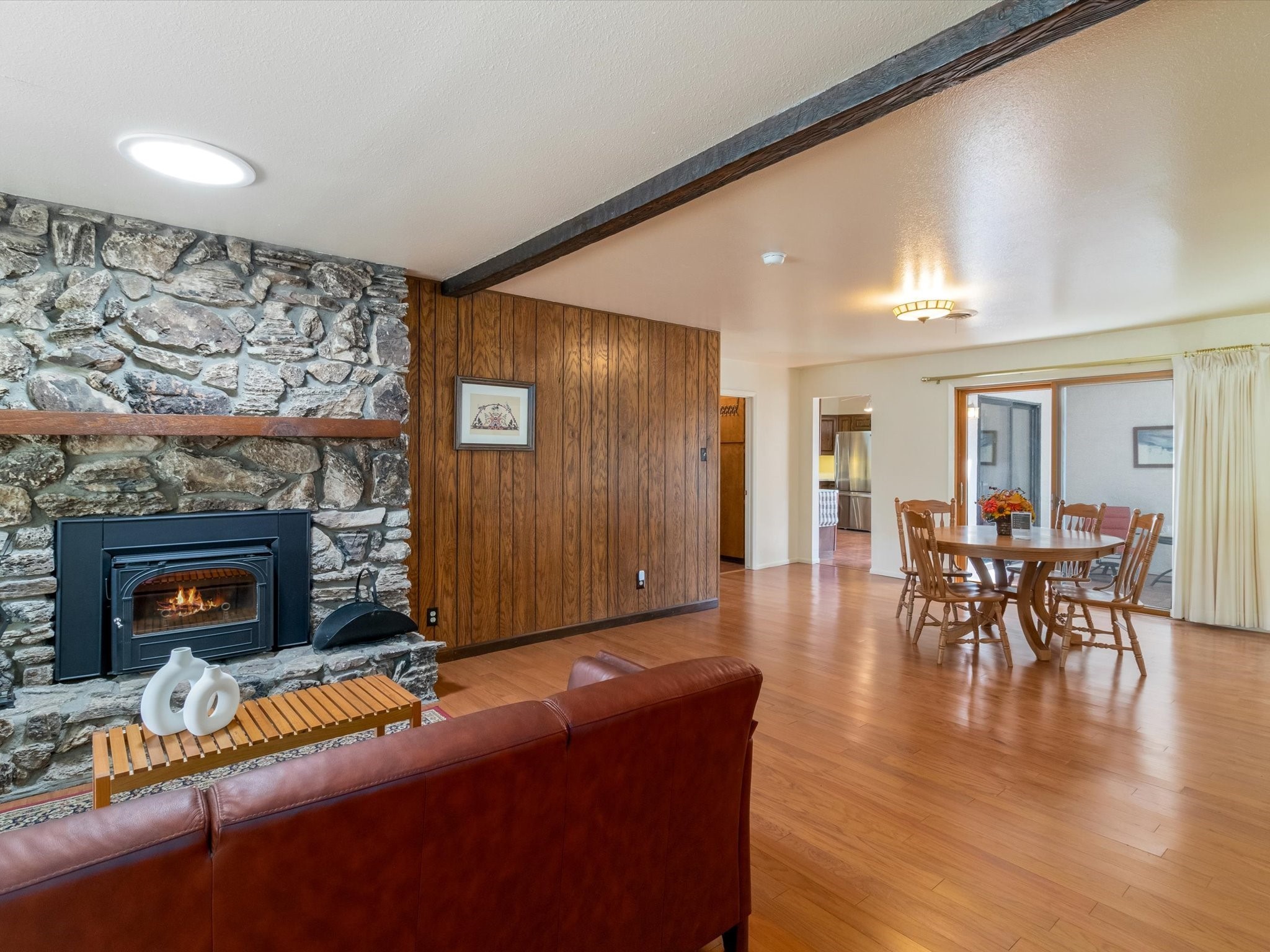 Living and dining room with a stone fireplace, wood-paneled wall, and hardwood floors.