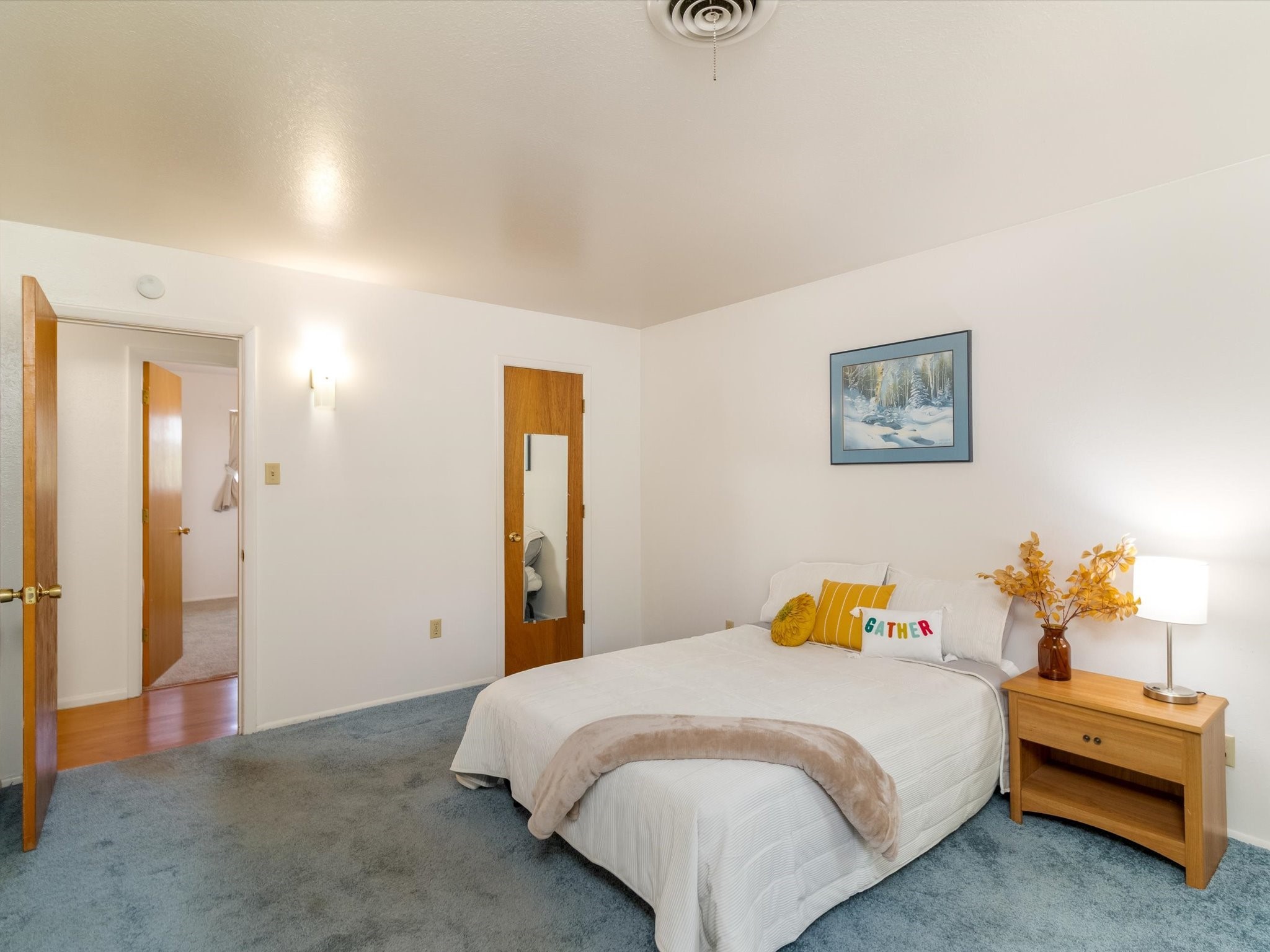 Bedroom with a white bed, blue-gray carpet, and wooden nightstand.