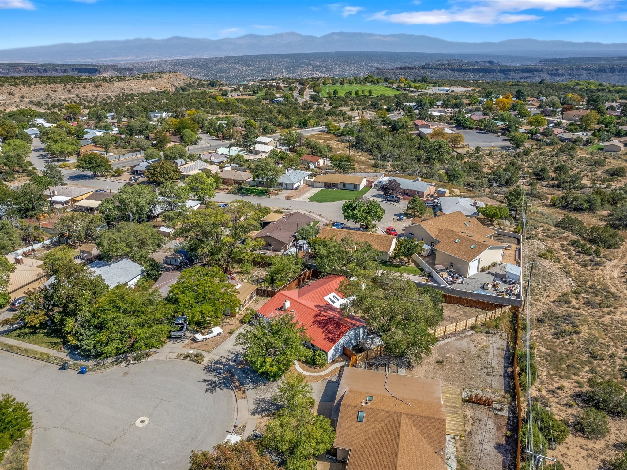 Aerial view of a red-roofed home among neighborhood houses, with distant mountains.