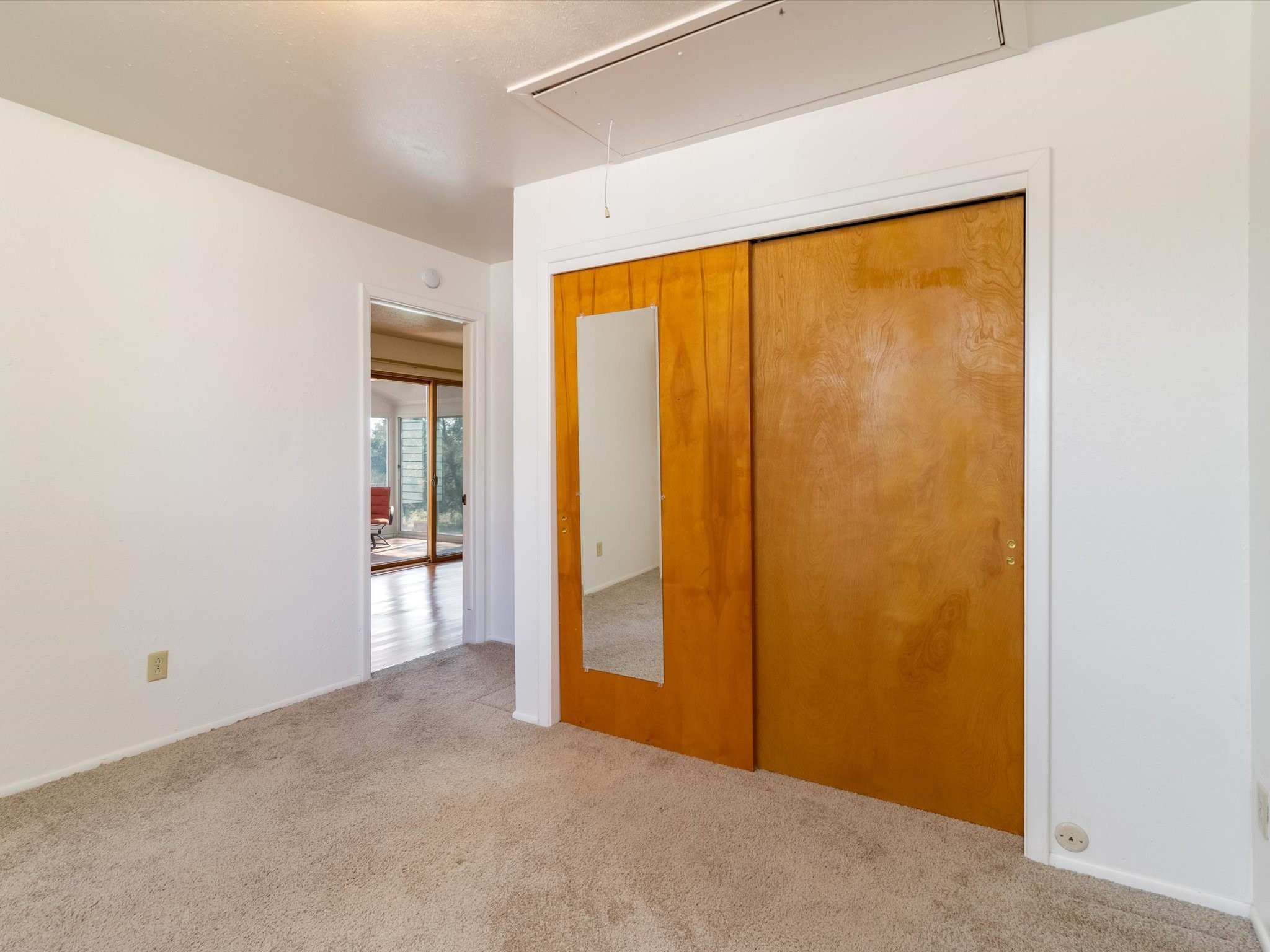 Empty carpeted bedroom with honey-colored sliding closet doors and a full-length mirror.