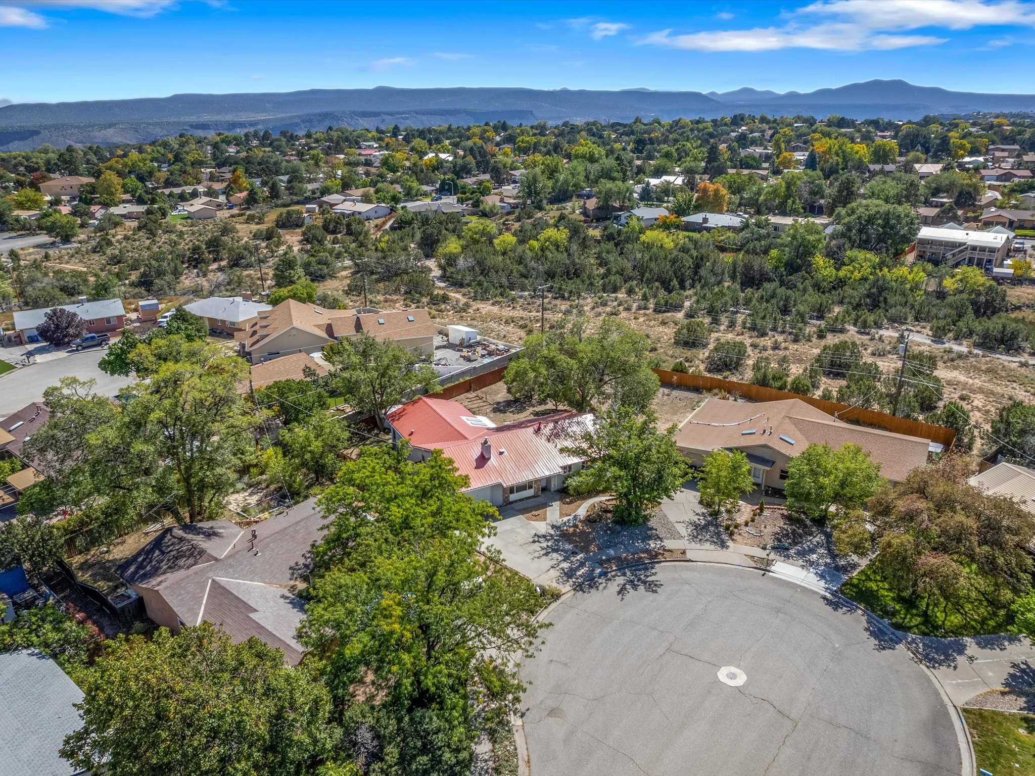 Aerial view of a red-roofed home near a cul-de-sac, with neighborhood homes and mountains beyond.