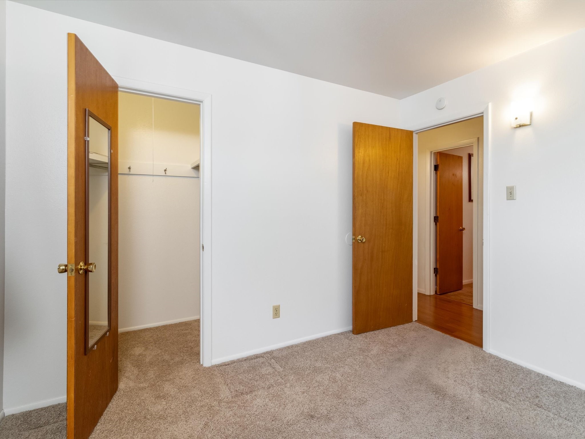 Unfurnished carpeted bedroom with a mirrored closet door and open hallway door.