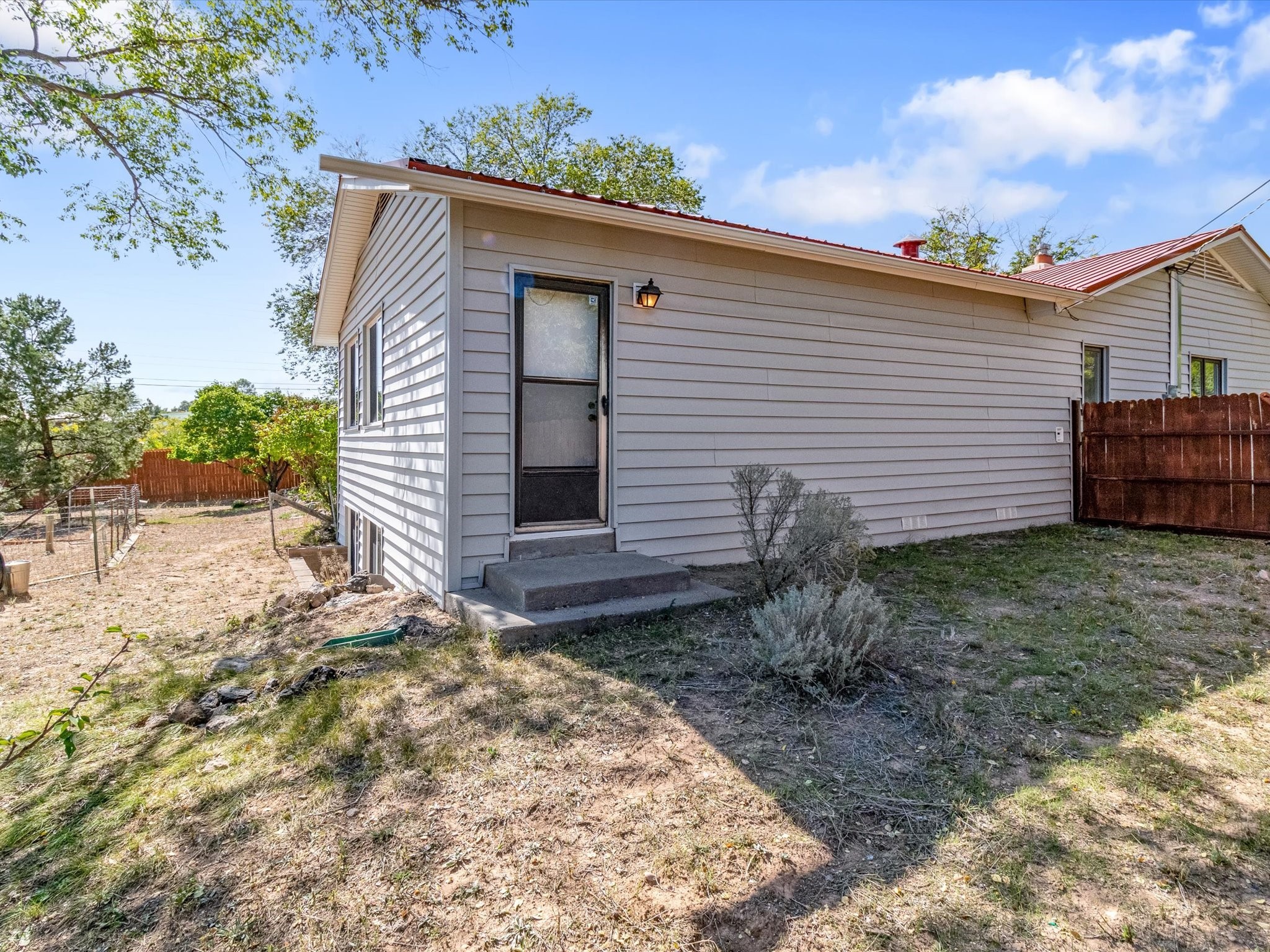 Gray-sided house with a screened rear door, concrete steps, red metal roof, and fenced yard.