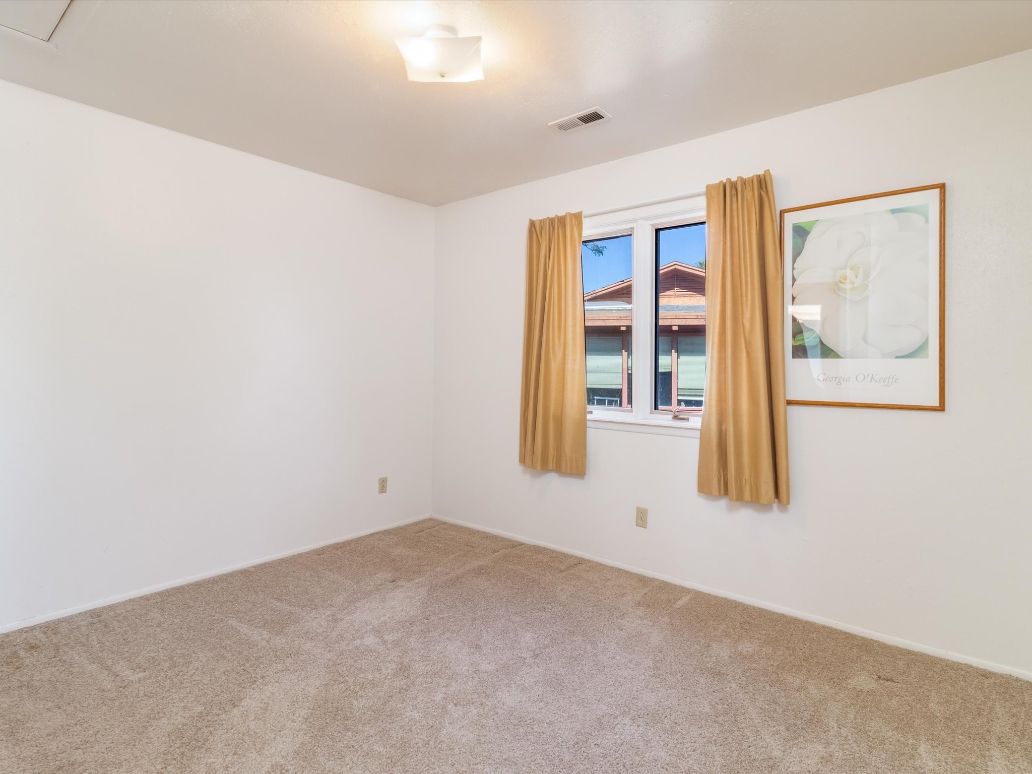 Empty carpeted room with gold curtains and framed floral artwork beside the window.