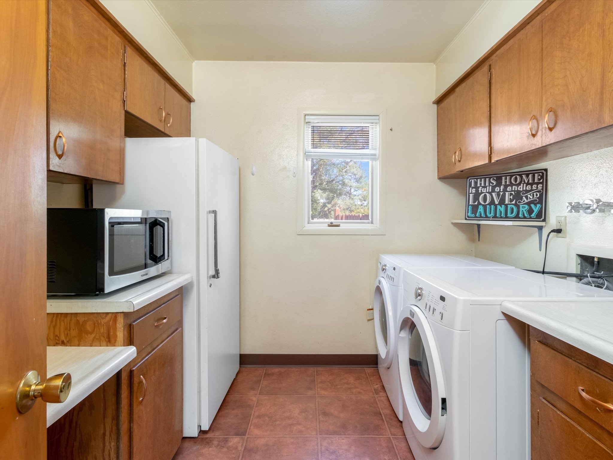 Laundry room with front-loading washer and dryer, wood cabinets, refrigerator, and window.