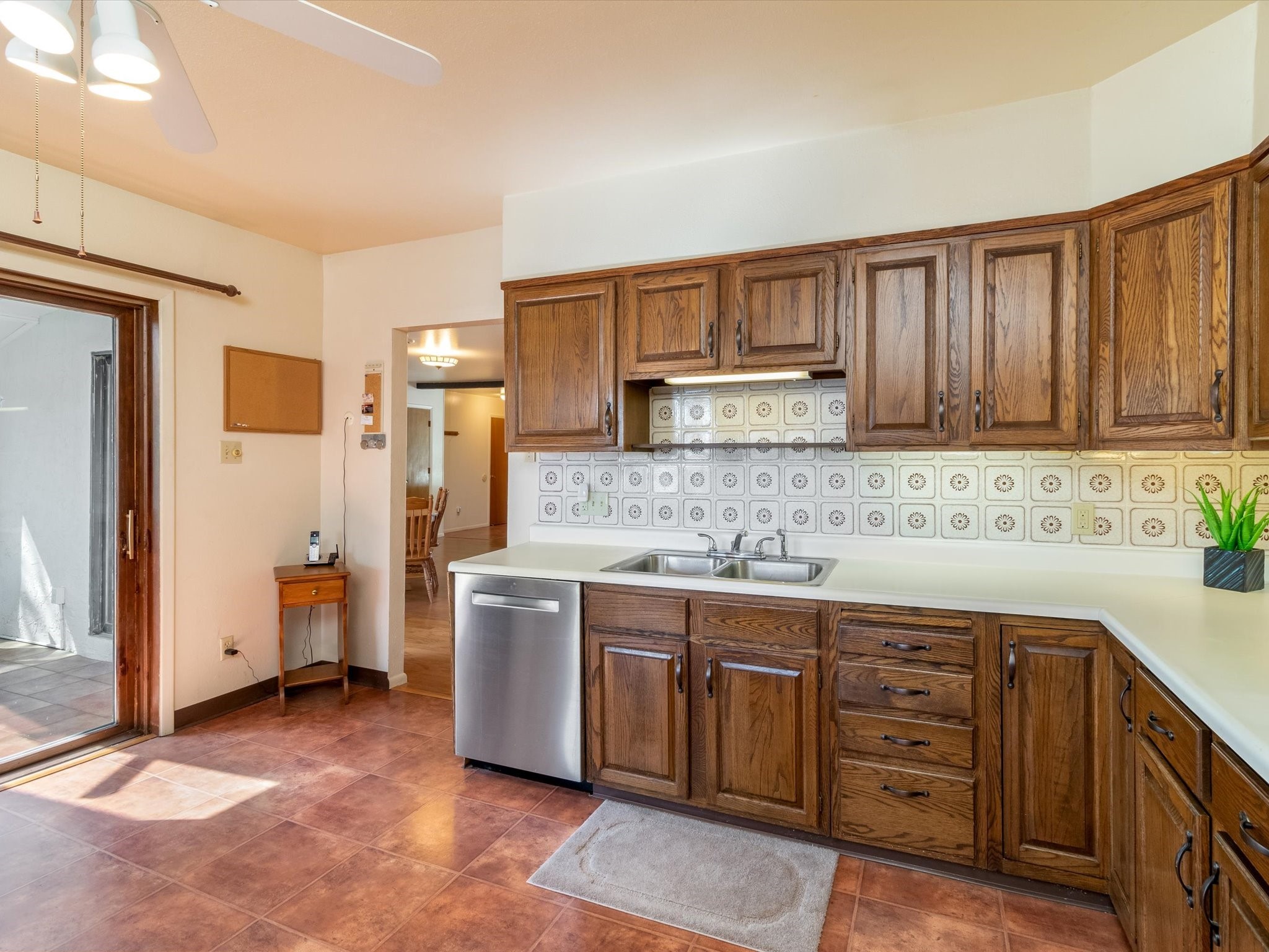 Kitchen with dark wood cabinets, patterned tile backsplash, white countertops, and stainless steel dishwasher.
