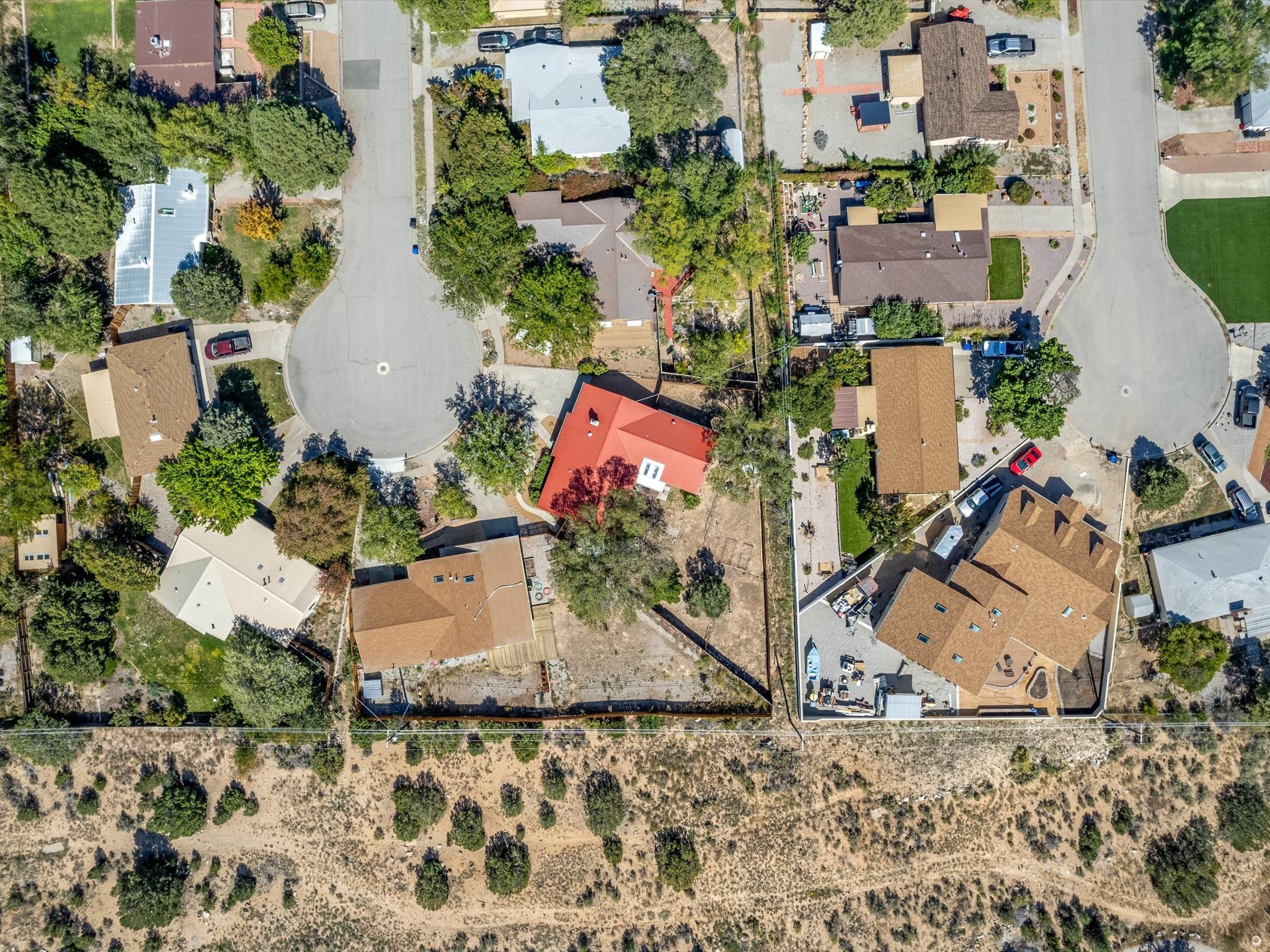 Aerial view of a residential neighborhood with cul-de-sacs, a red-roofed home, and dry open land.
