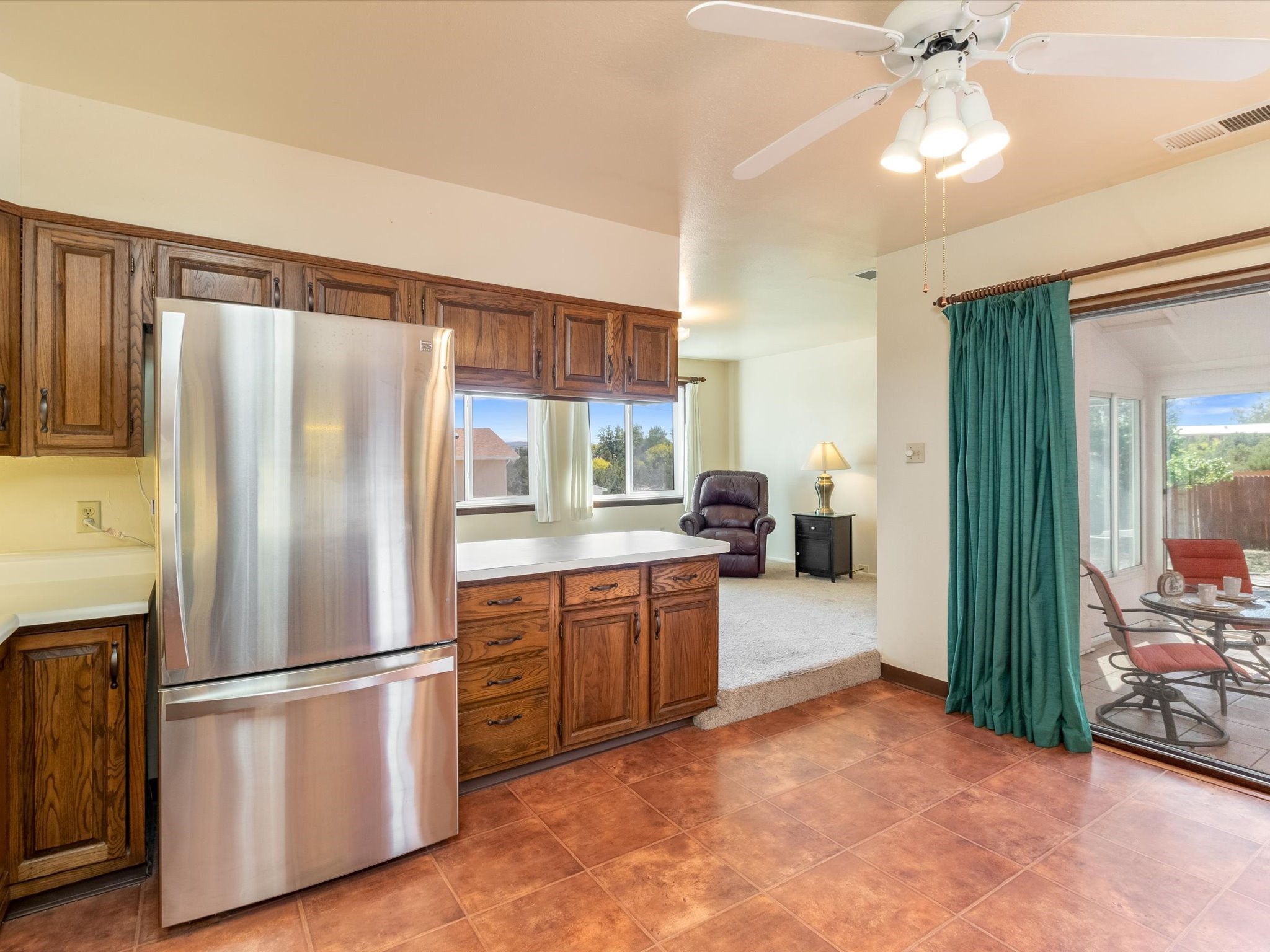 Kitchen with wood cabinets and stainless refrigerator, opening to a raised sitting area and patio.