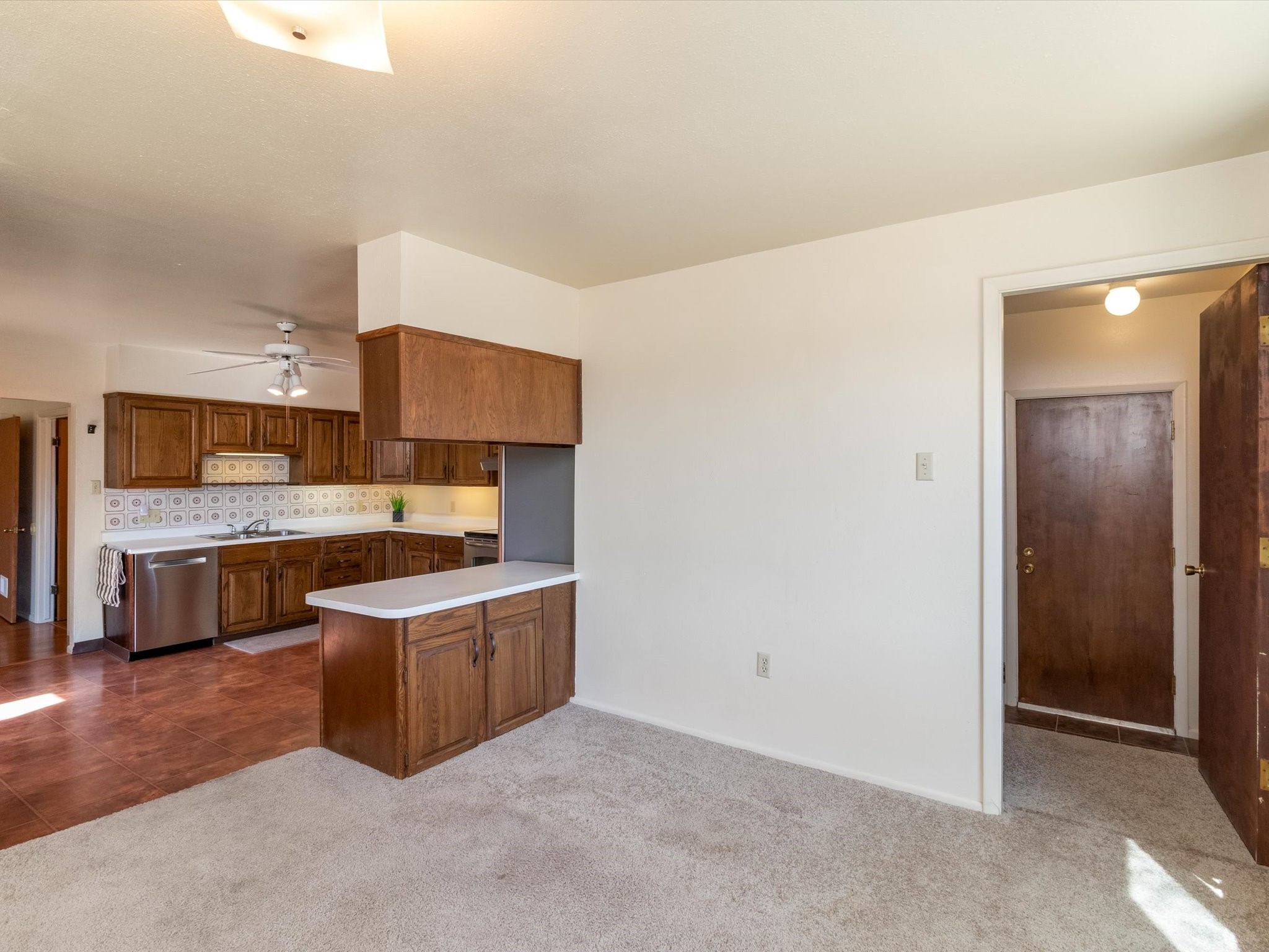 Kitchen with dark wood cabinets and peninsula adjoining an unfurnished carpeted living area.