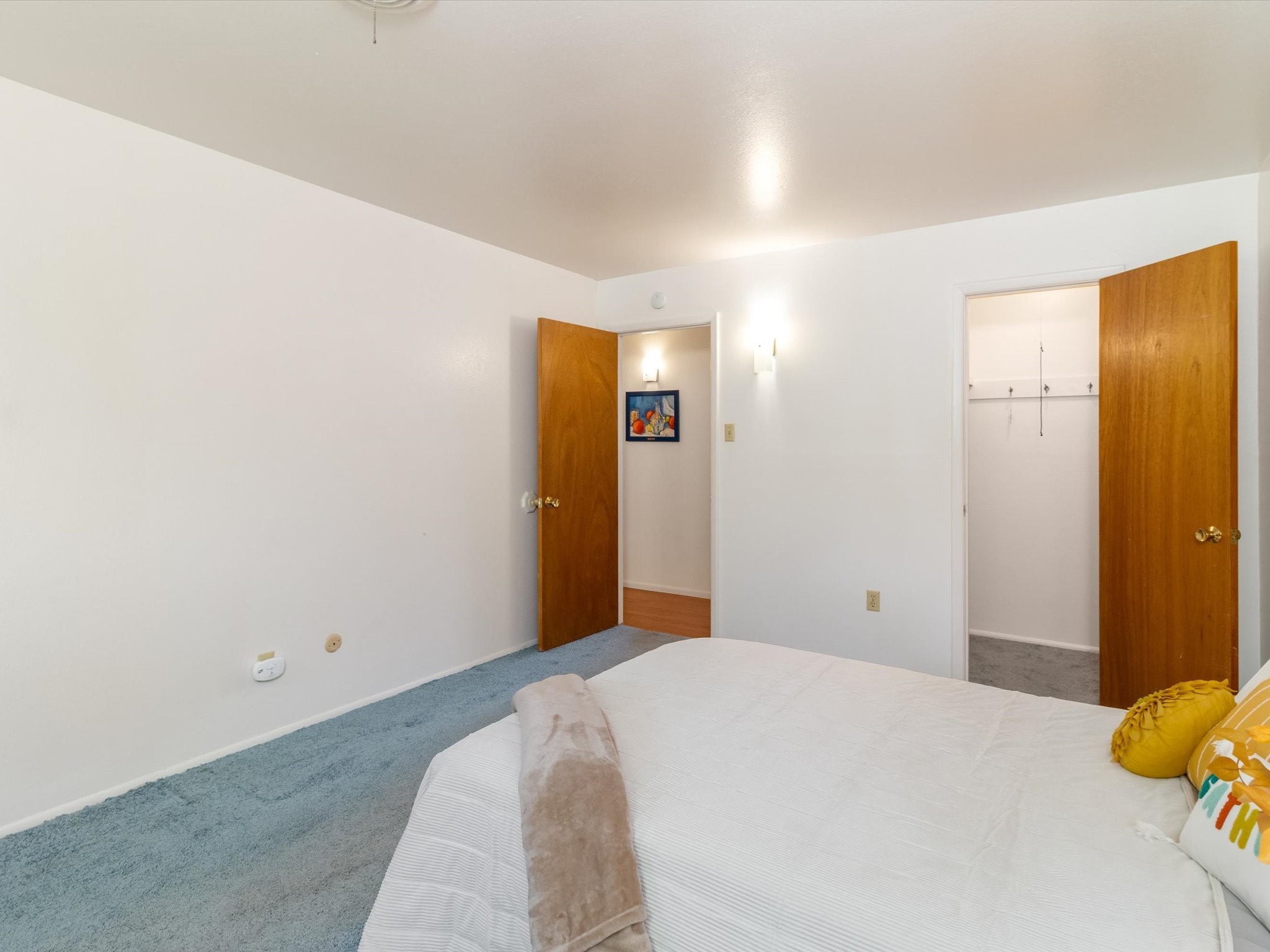 Bedroom with a white bed, blue carpet, and open wooden doors to adjoining rooms.