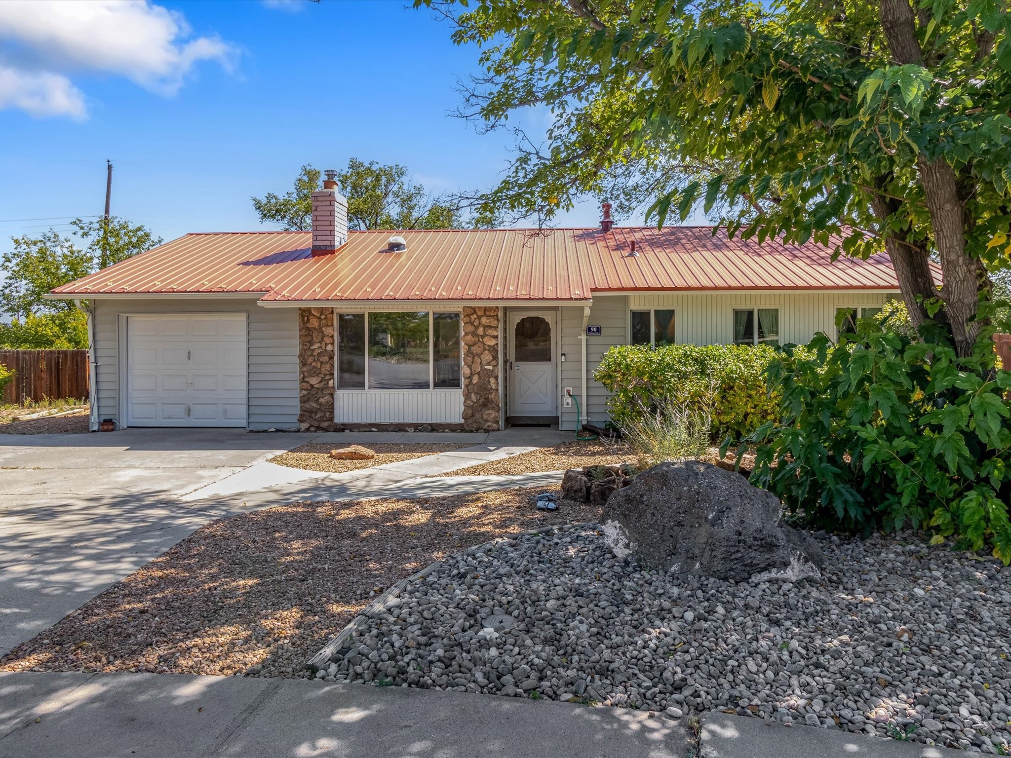 Single-story home with a red metal roof, attached garage, stone accents, and a rock-landscaped yard.