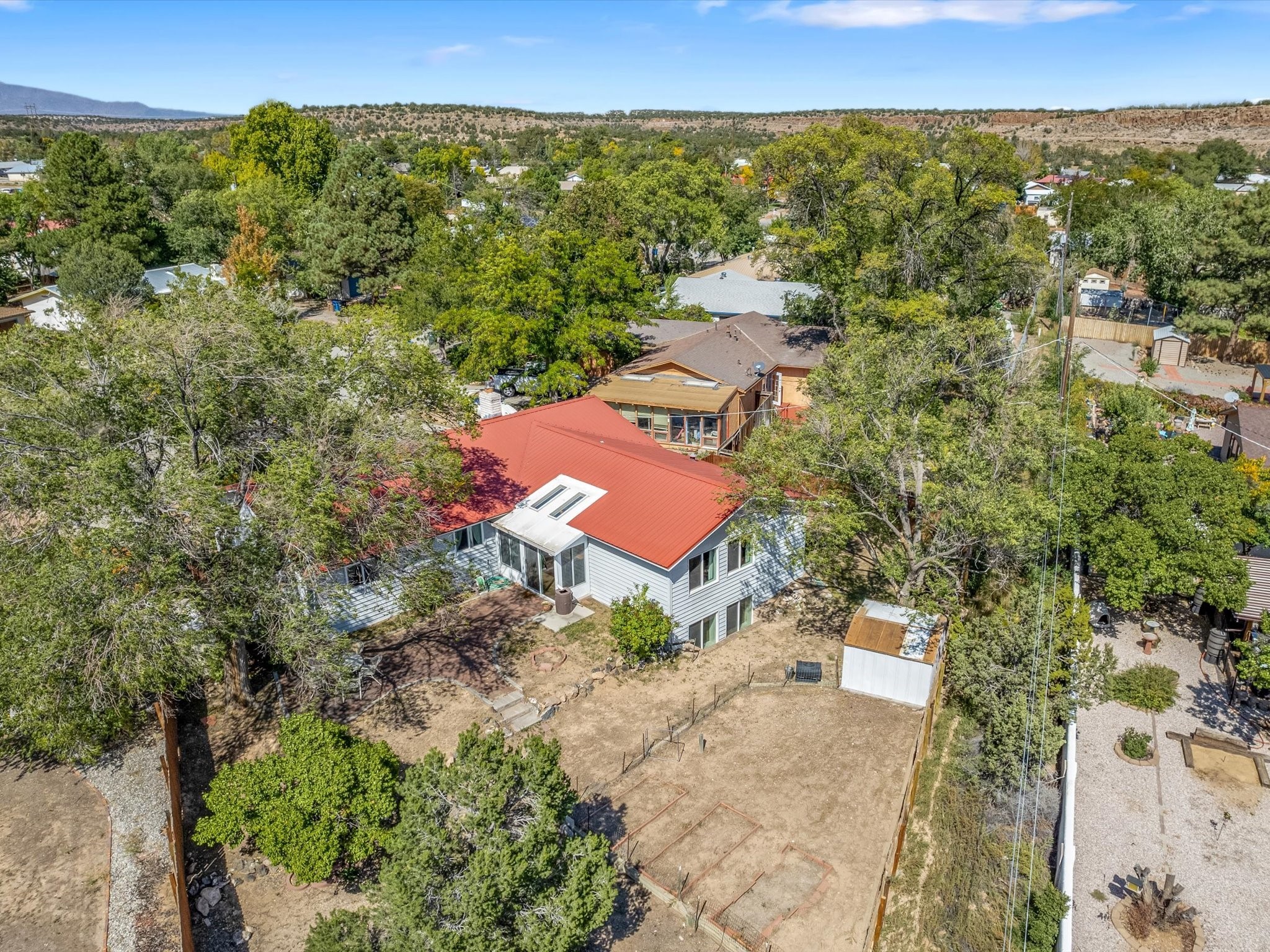 Aerial view of a light-colored house with a red roof, skylights, and a fenced yard.