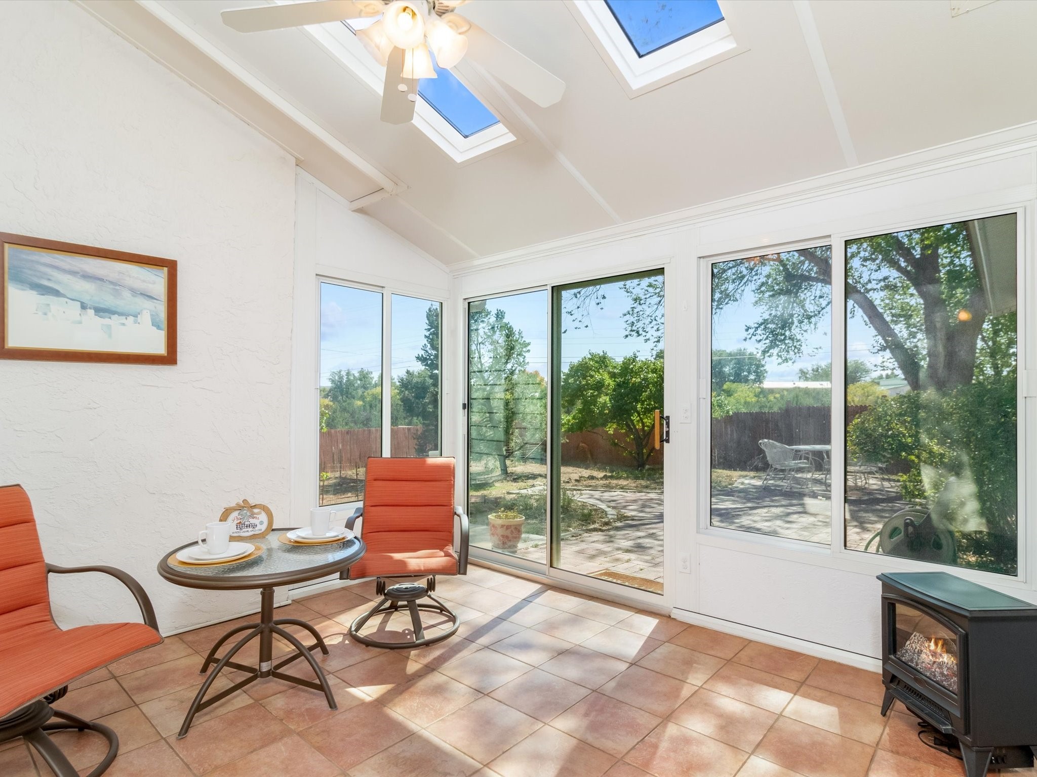 Sunroom with terracotta tile, orange chairs, skylights, and windows overlooking a leafy patio.