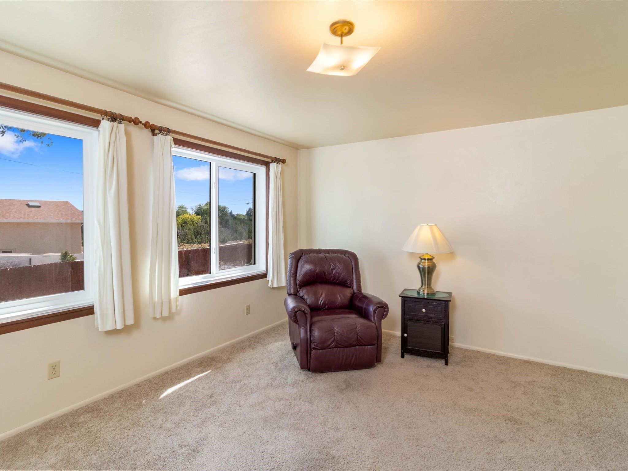 Carpeted sitting room with a burgundy recliner beside two curtained windows.