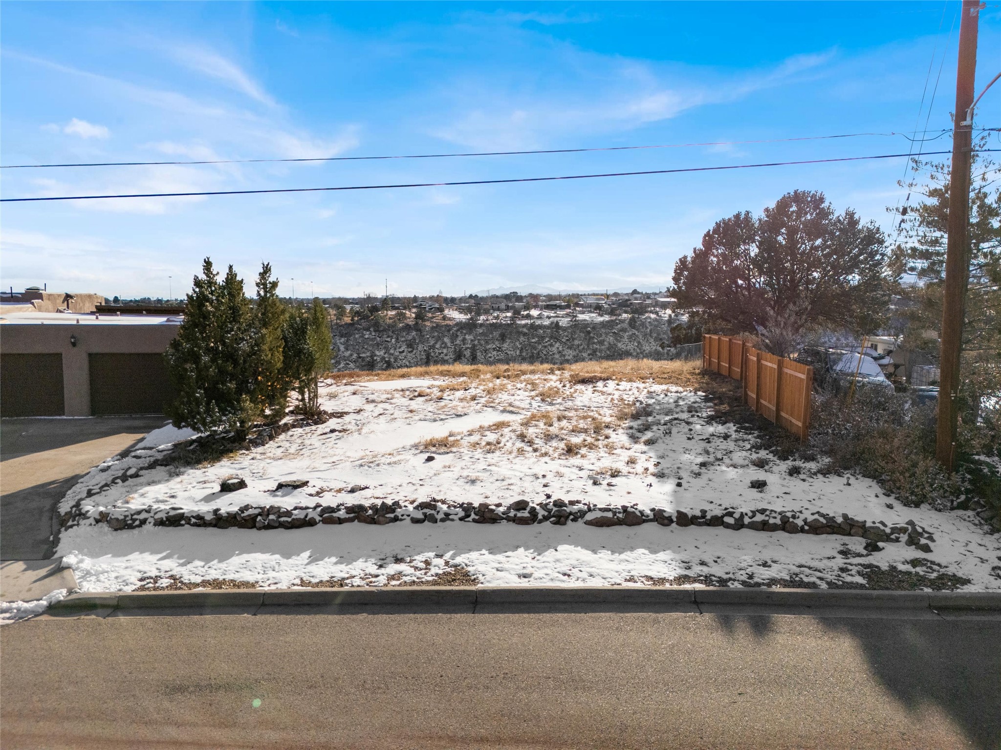 Snow-covered residential yard with a stone border, wooden fence, and distant mountain views.