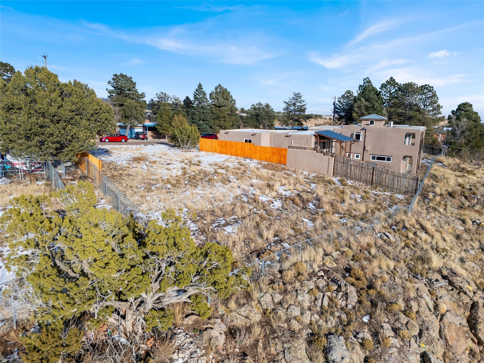 Tan Southwestern-style home beside a rocky, fenced lot with juniper trees and patches of snow.