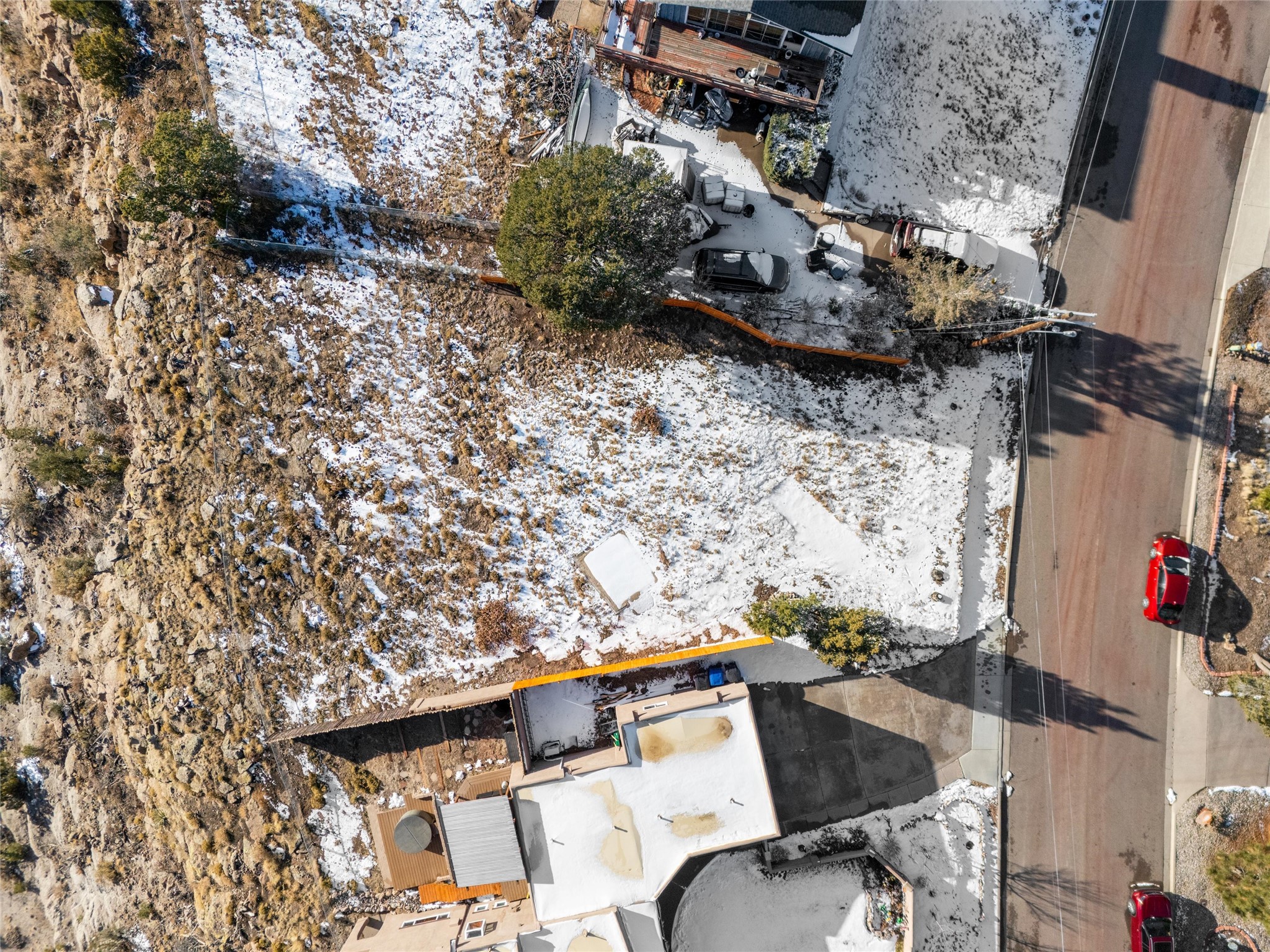 Aerial view of a snow-dusted property beside a road and rocky hillside.