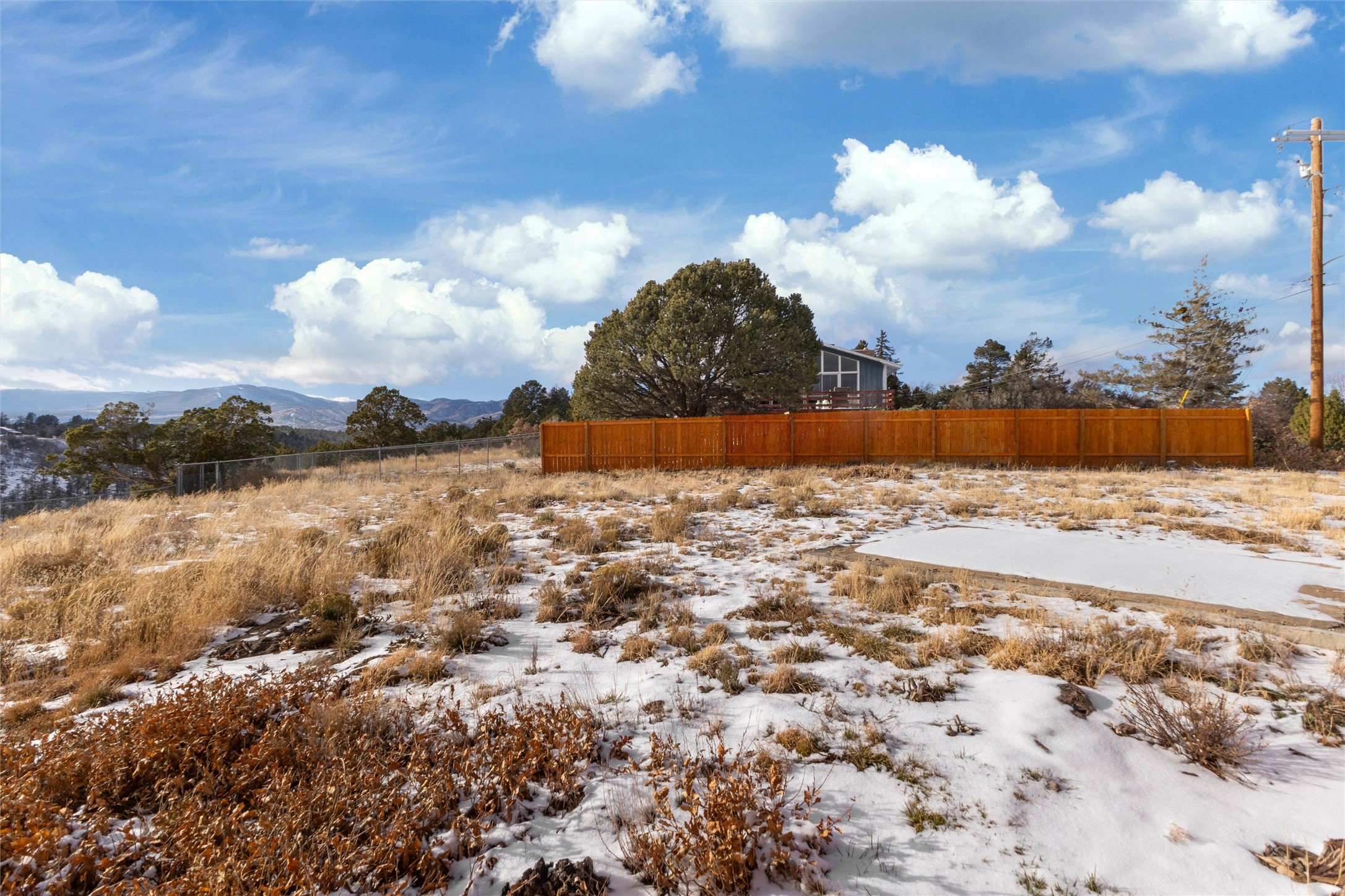 Snow-dusted property lot with a concrete pad, wooden fence, and mountain views.