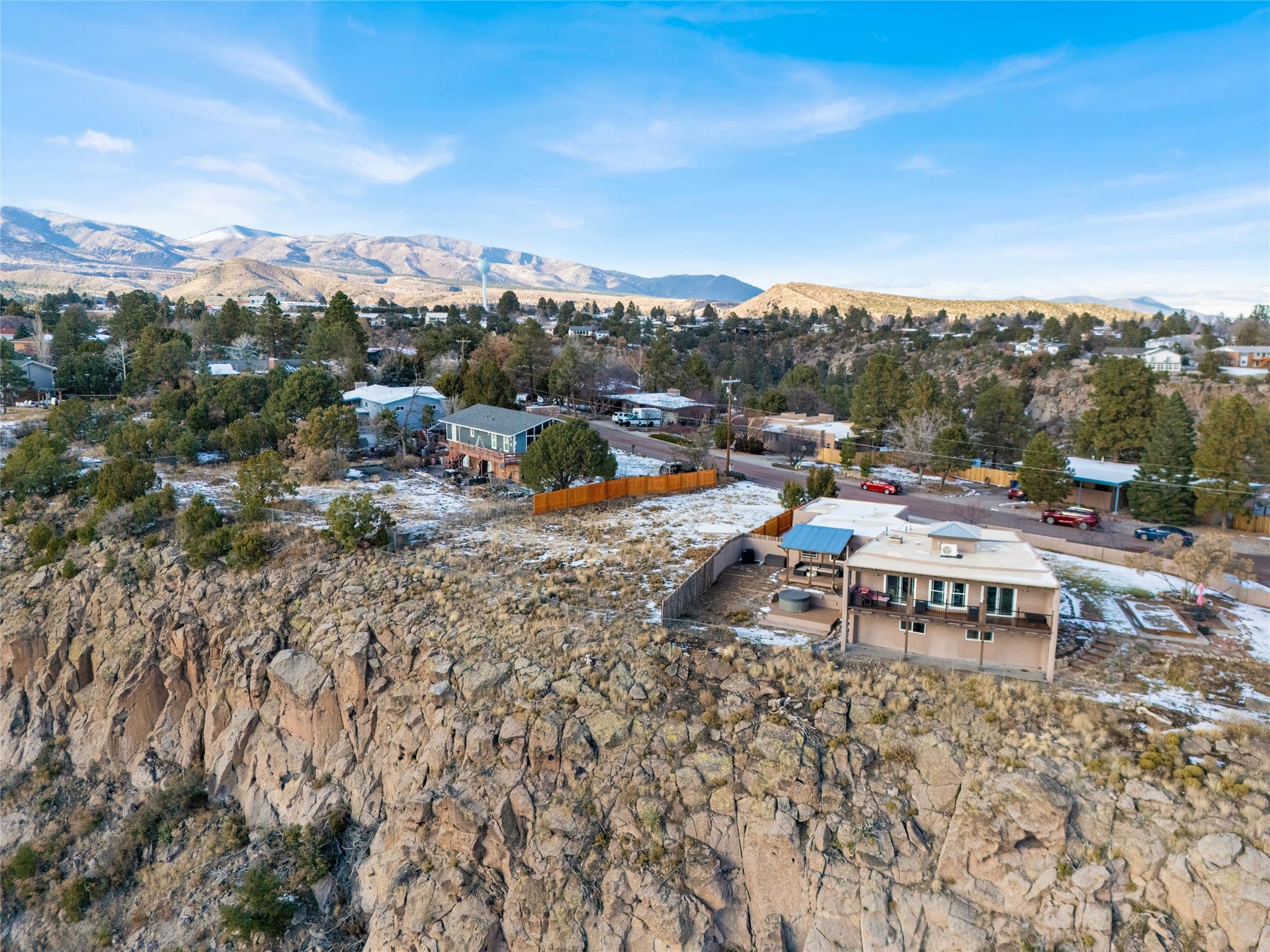 Home perched above a rocky cliff, with neighboring homes and snow-dusted mountains beyond.