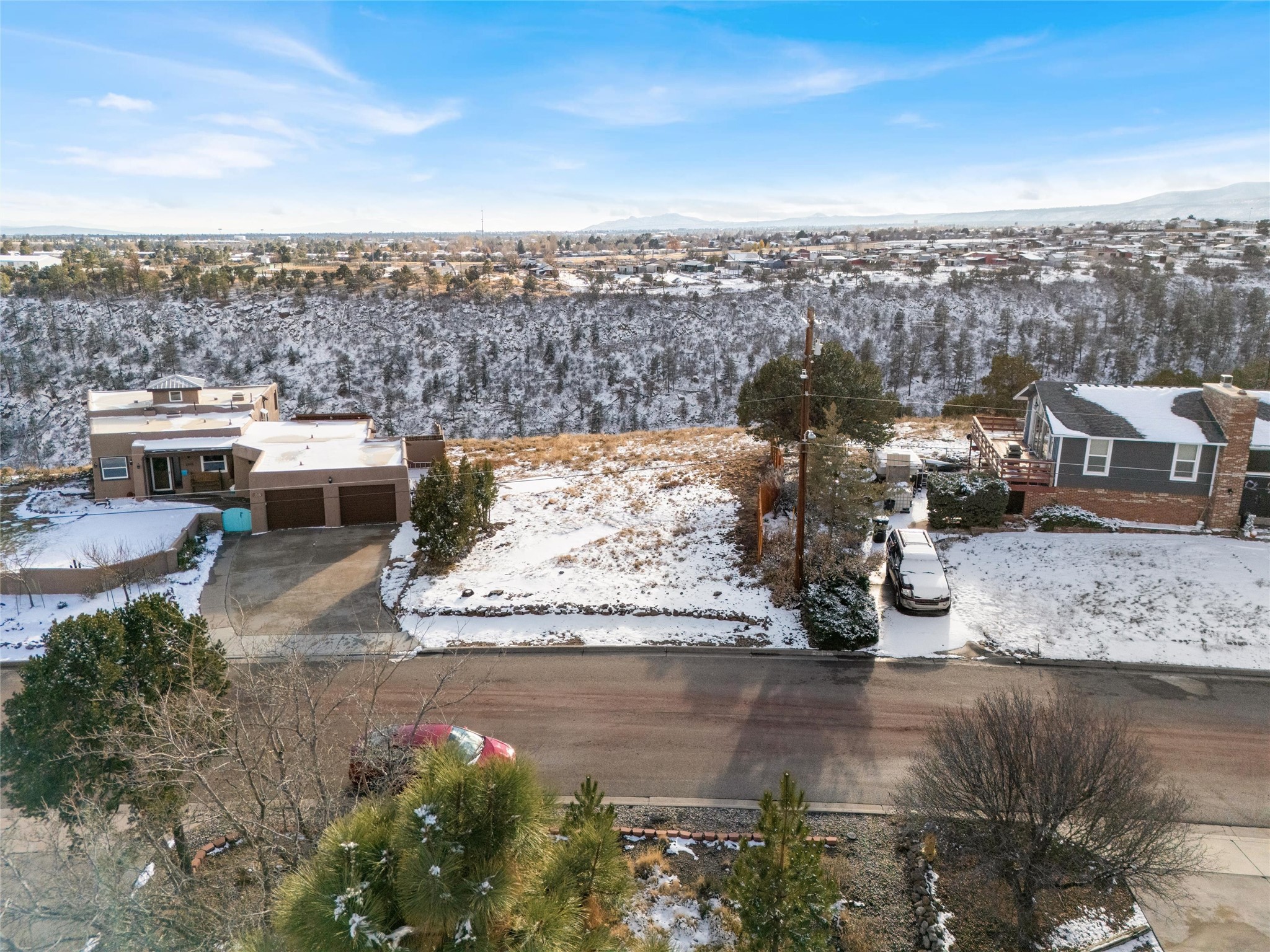 Aerial view of a flat-roof home with a two-car garage beside a snow-covered canyon.