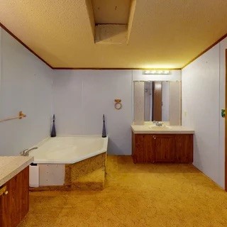 Bathroom with a corner bathtub and separate wood vanity beneath a low ceiling.
