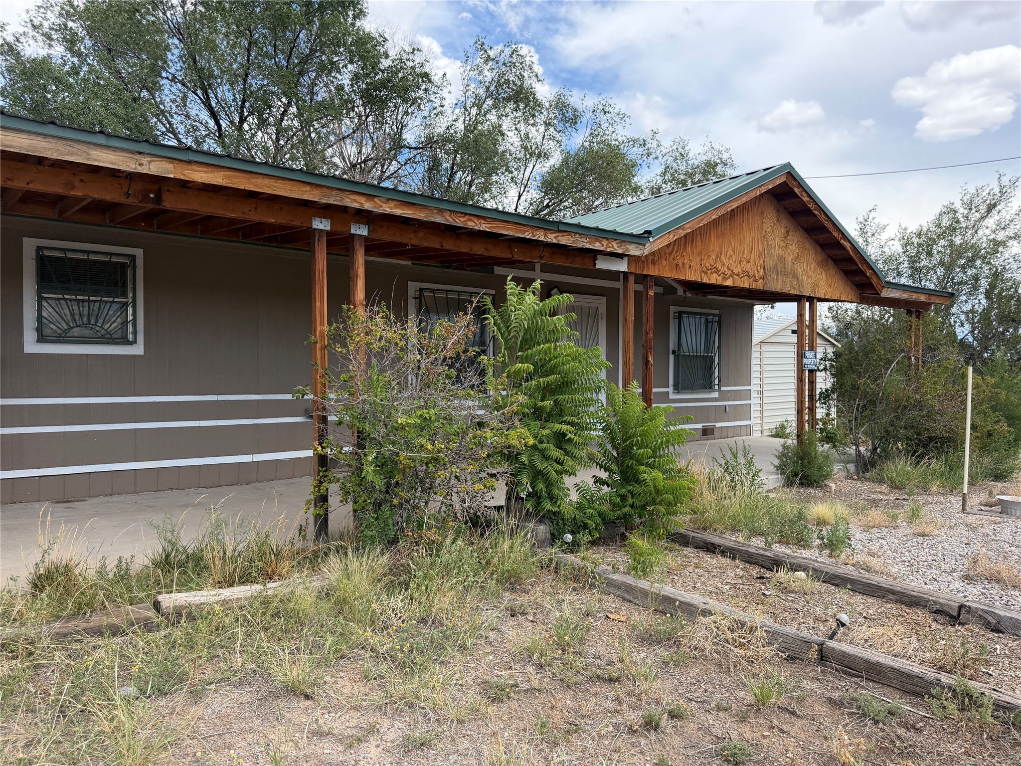 Single-story home with a deep wooden-post porch, green metal roof, and gravel landscaping.
