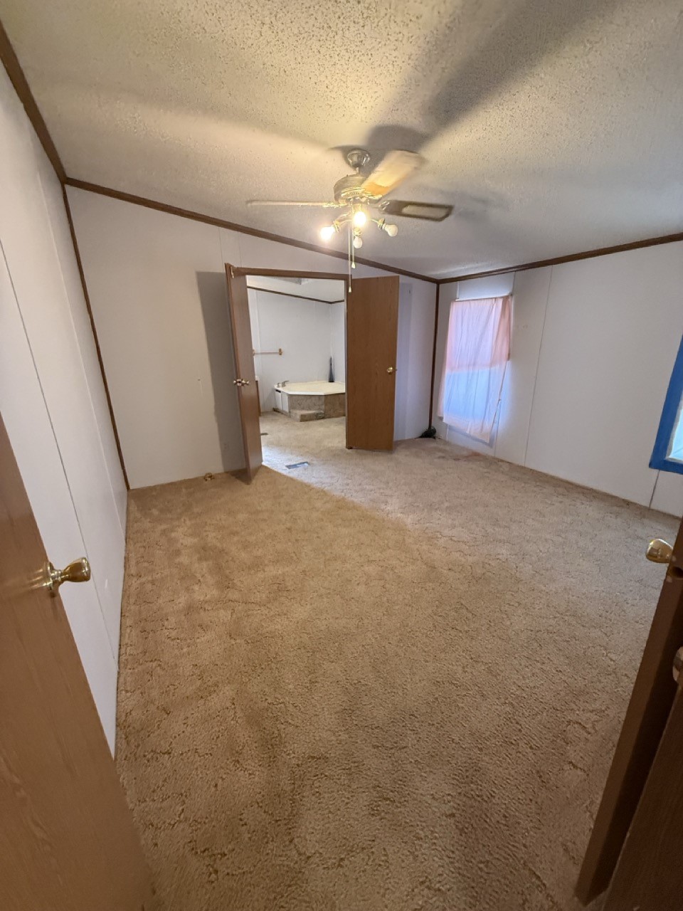 Empty carpeted bedroom with a ceiling fan and an open doorway to a bathroom with a corner tub.