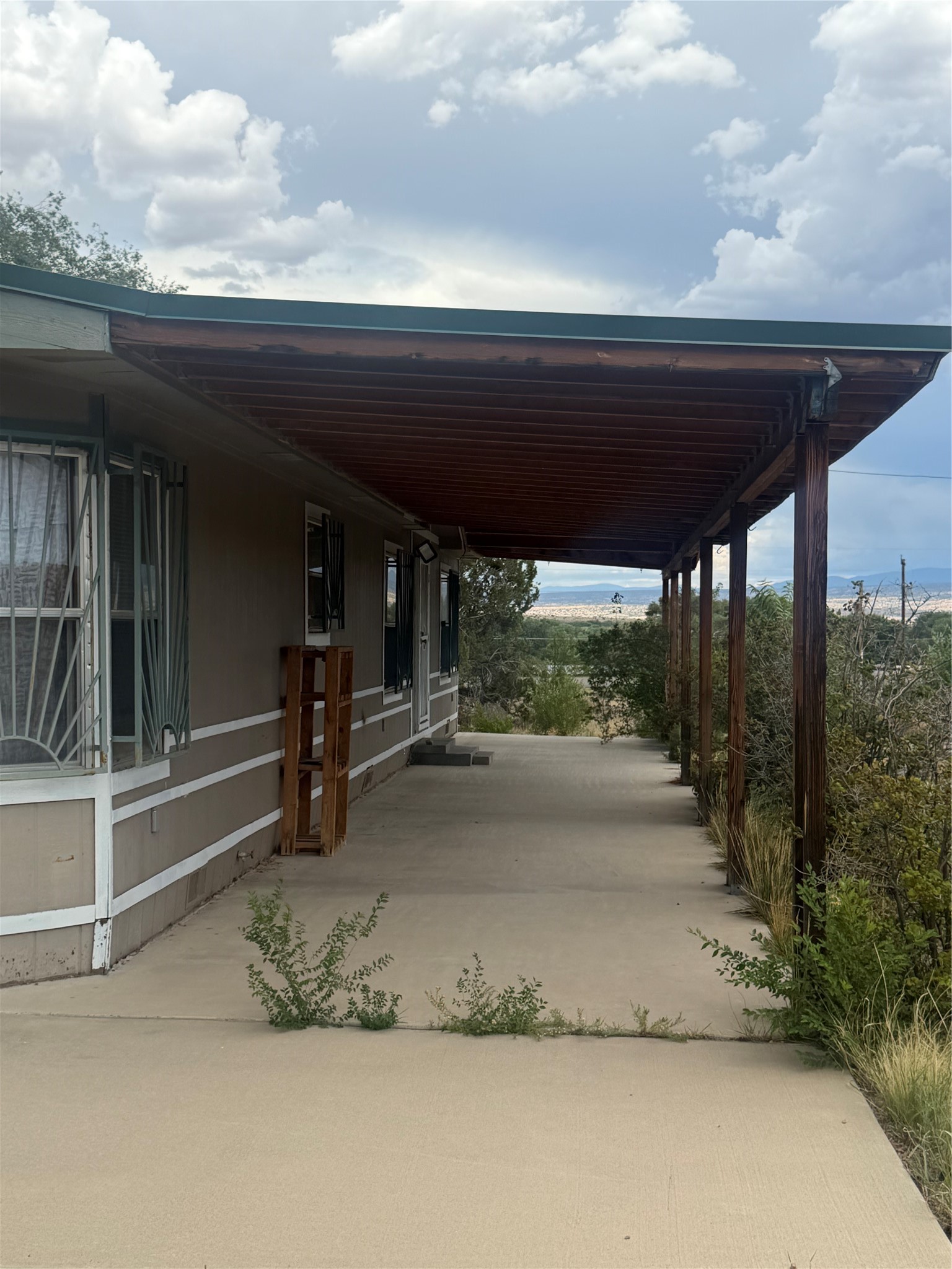 Concrete porch beside a home, shaded by a wide wooden roof with distant hills beyond.