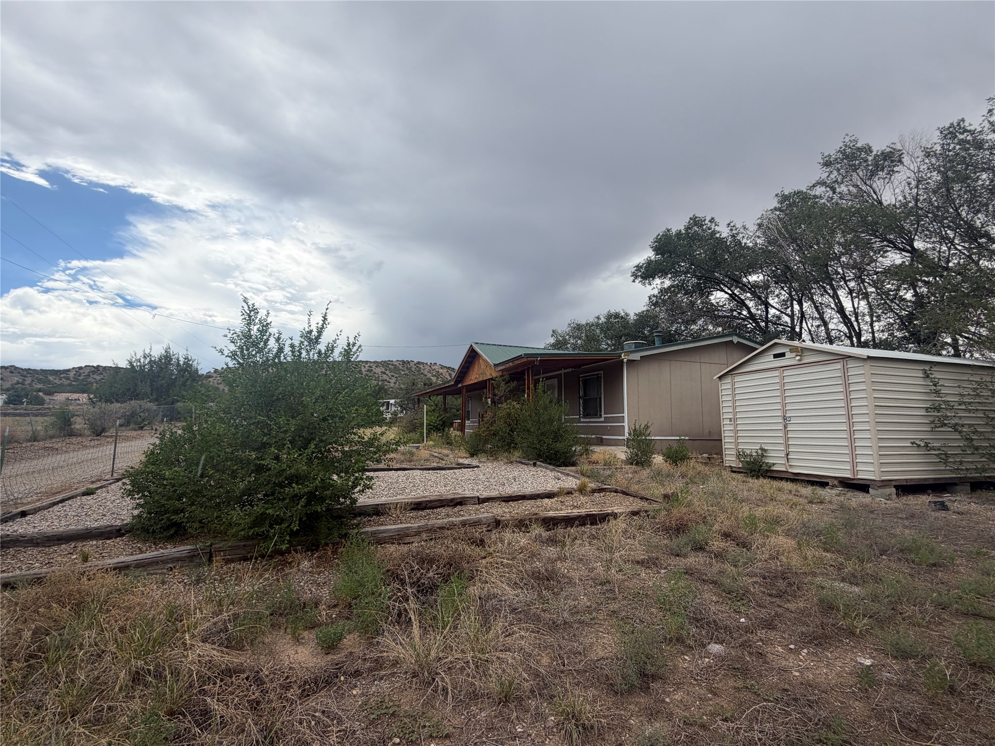 Single-story home with a covered porch and metal shed beside a dry, overgrown gravel yard.