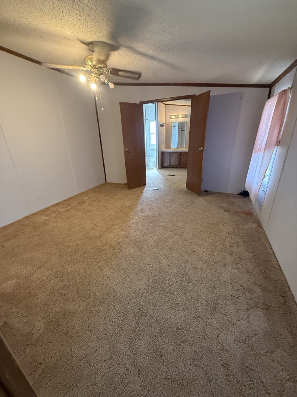 Unfurnished carpeted room with a ceiling fan, pink window curtains, and an open doorway to a bathroom.