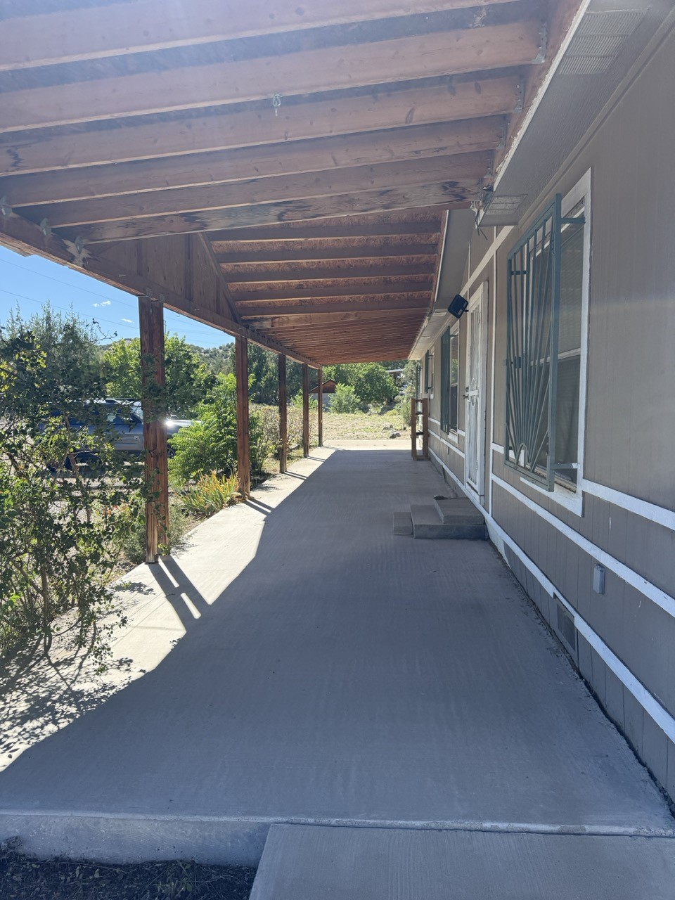 Covered concrete porch with a long wooden awning and barred windows along the house.