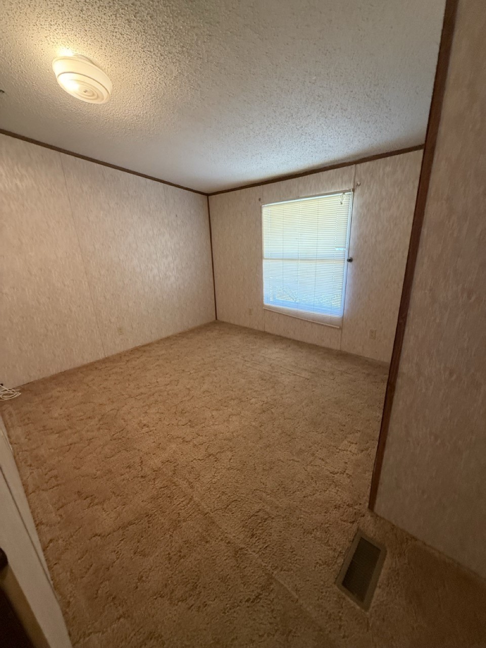 Empty bedroom with beige carpet, dark wood trim, and a window with closed blinds.