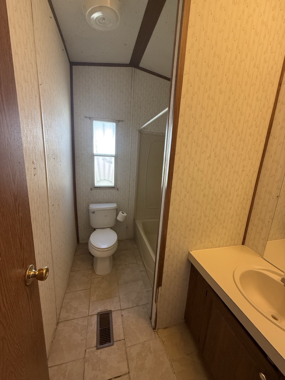Narrow bathroom with a toilet beneath a tall window, bathtub, and sink vanity.