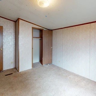 Empty carpeted room with an open closet and wood trim.