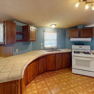 Kitchen with a curved tiled peninsula, reddish wood cabinets, and a white range.