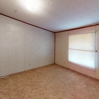 Vacant room with brown carpet, beige walls, and a window with closed blinds.