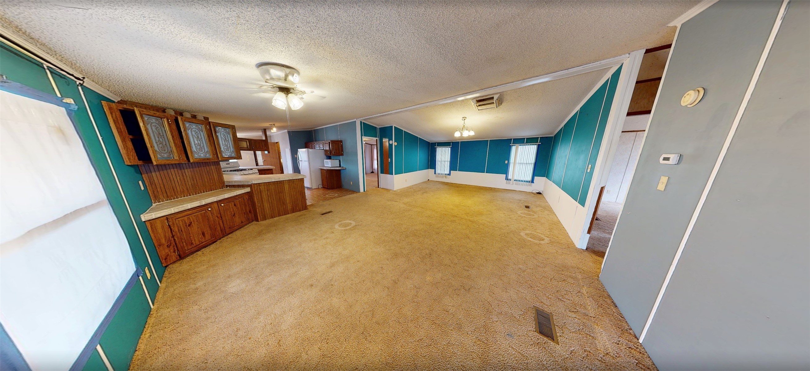 Vacant living room with teal paneled walls, tan carpet, and built-in wooden cabinetry beside the kitchen.