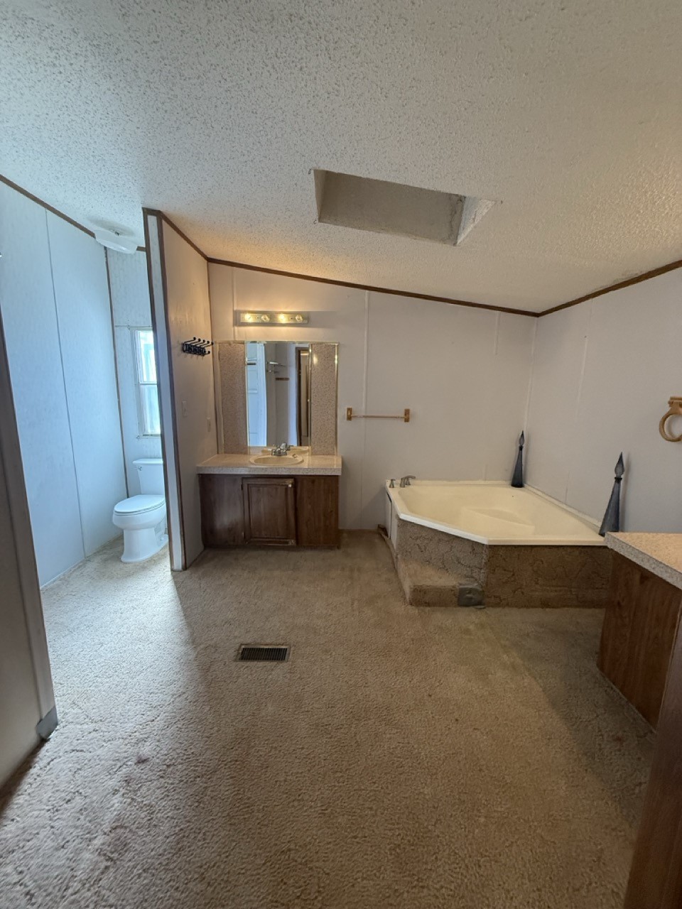 Bathroom with a large corner tub, wood vanity, and toilet alcove.