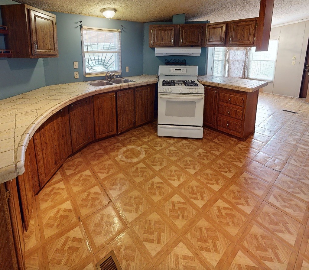 Kitchen with curved tiled counters, dark wood cabinets, a white gas range, and patterned flooring.