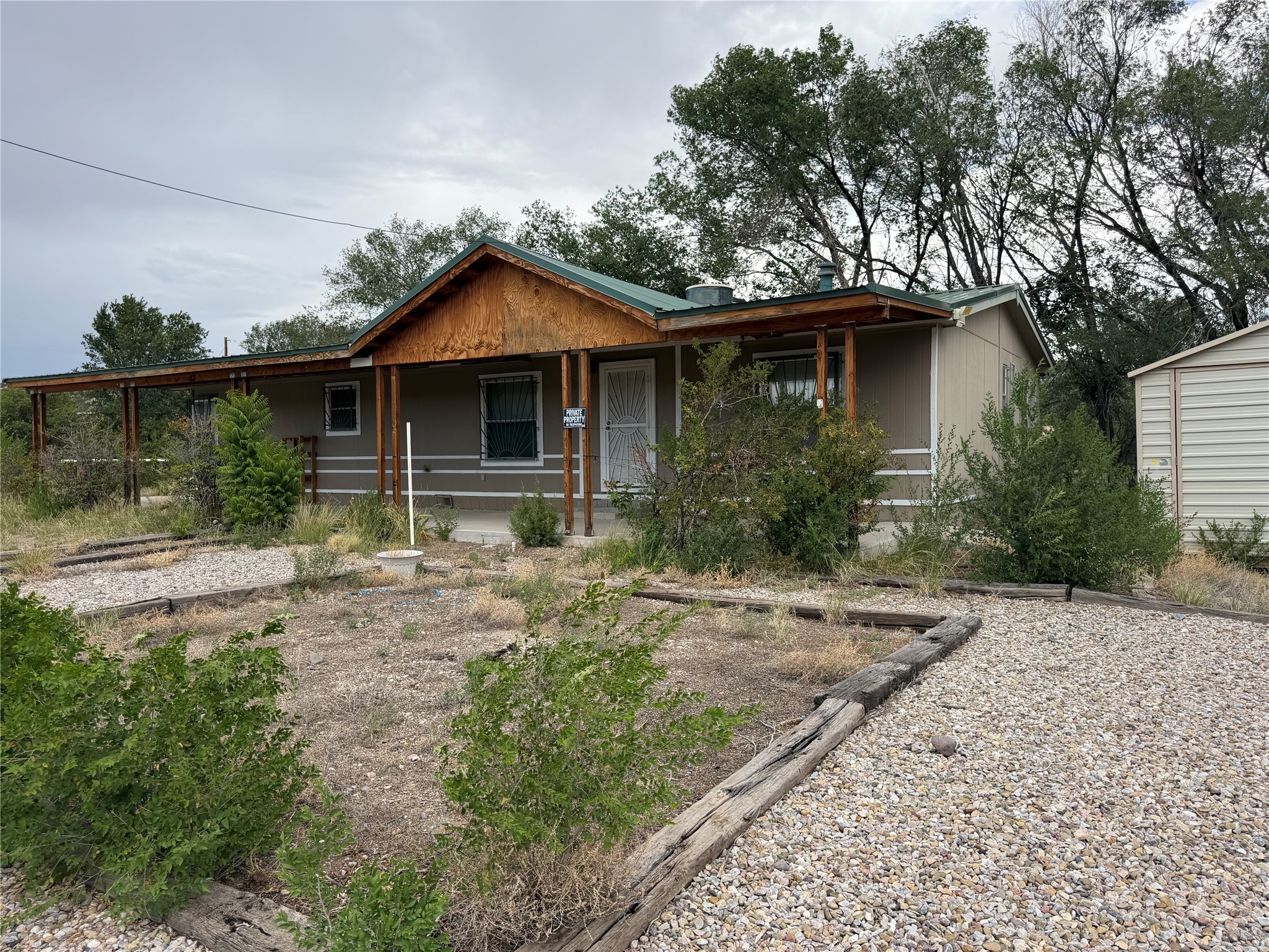 Single-story home with a broad covered porch, green roof, and gravel front yard.