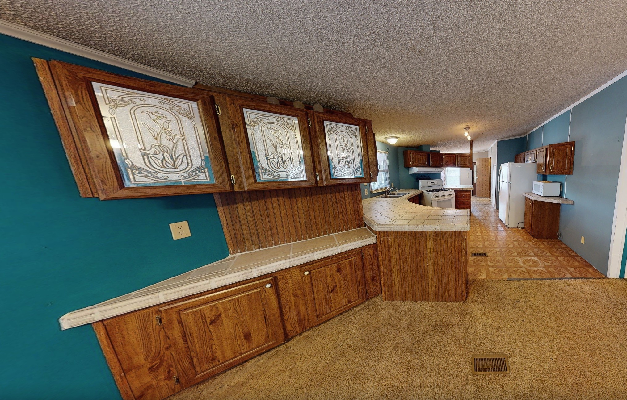 Kitchen with teal walls, decorative wood cabinets, tiled peninsula, and white appliances.