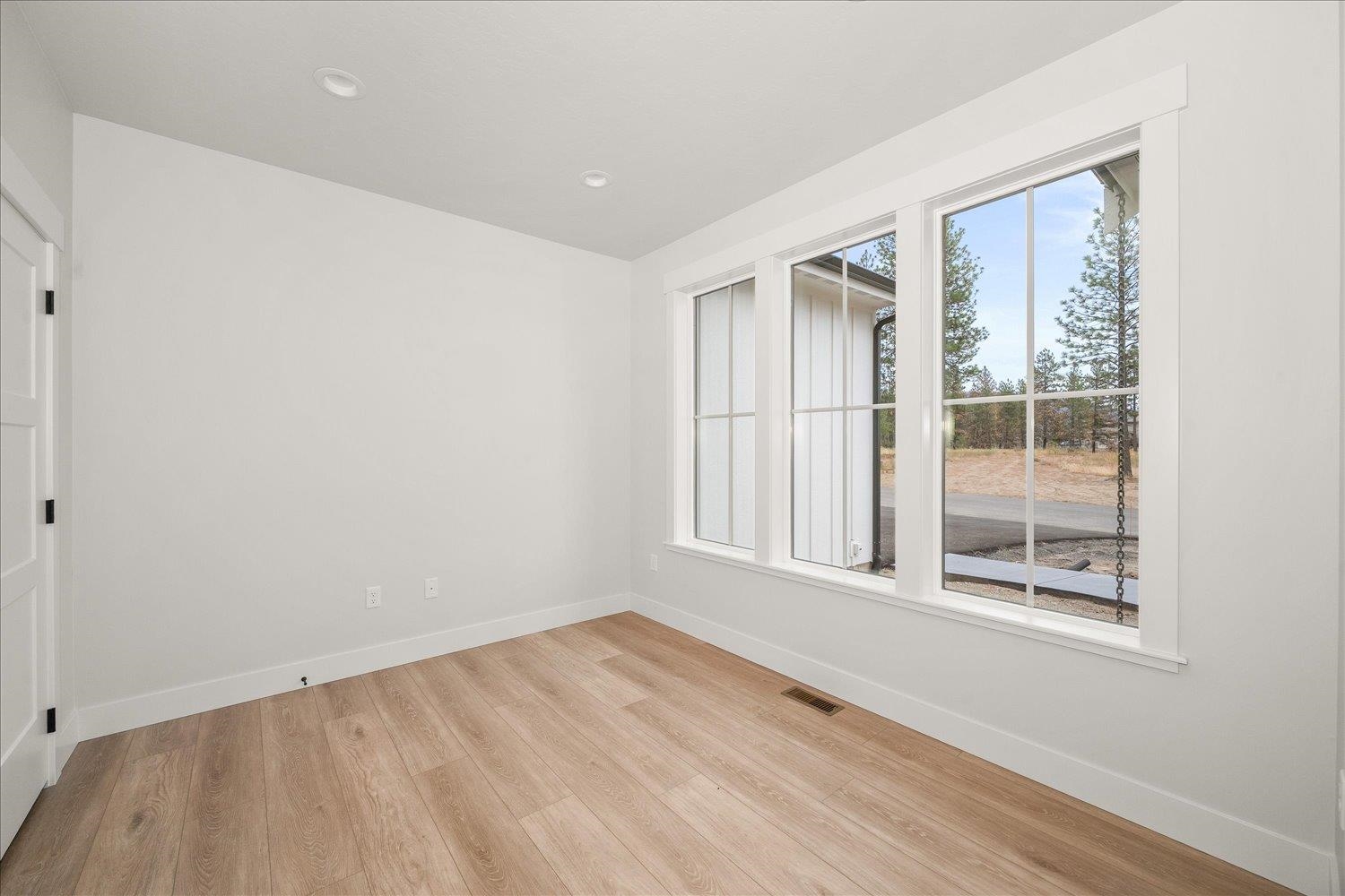 Empty room with light wood floors and large windows overlooking trees.