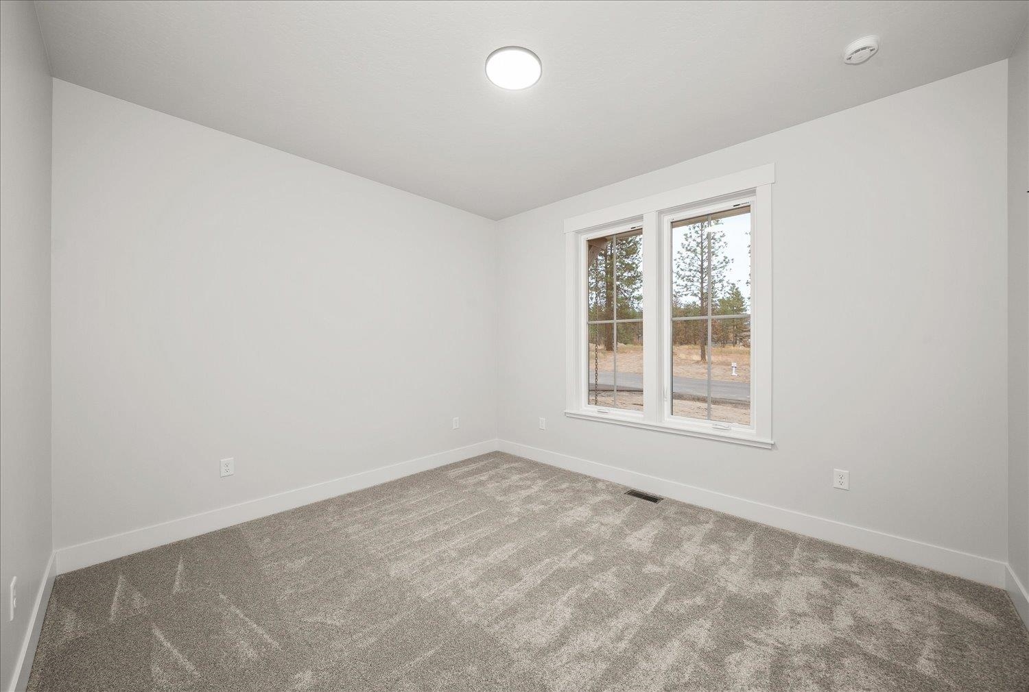 Empty bedroom with gray carpet and a large window overlooking trees.