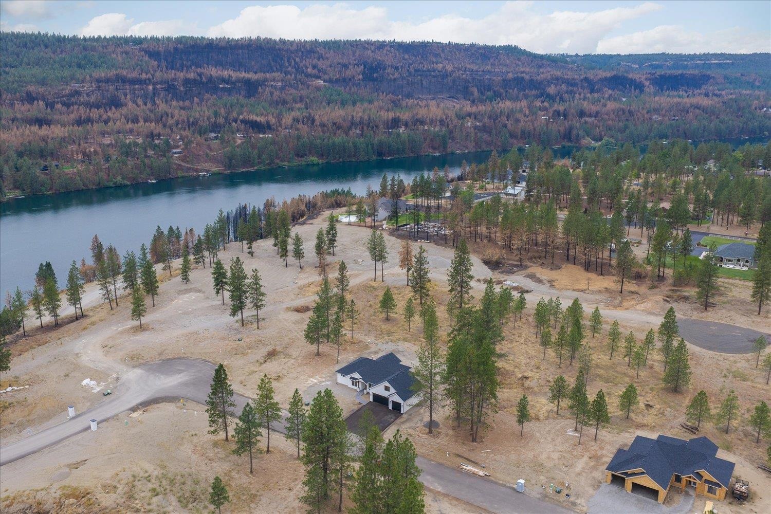 Aerial view of wooded riverfront lots, roads, scattered pines, and homes under construction.