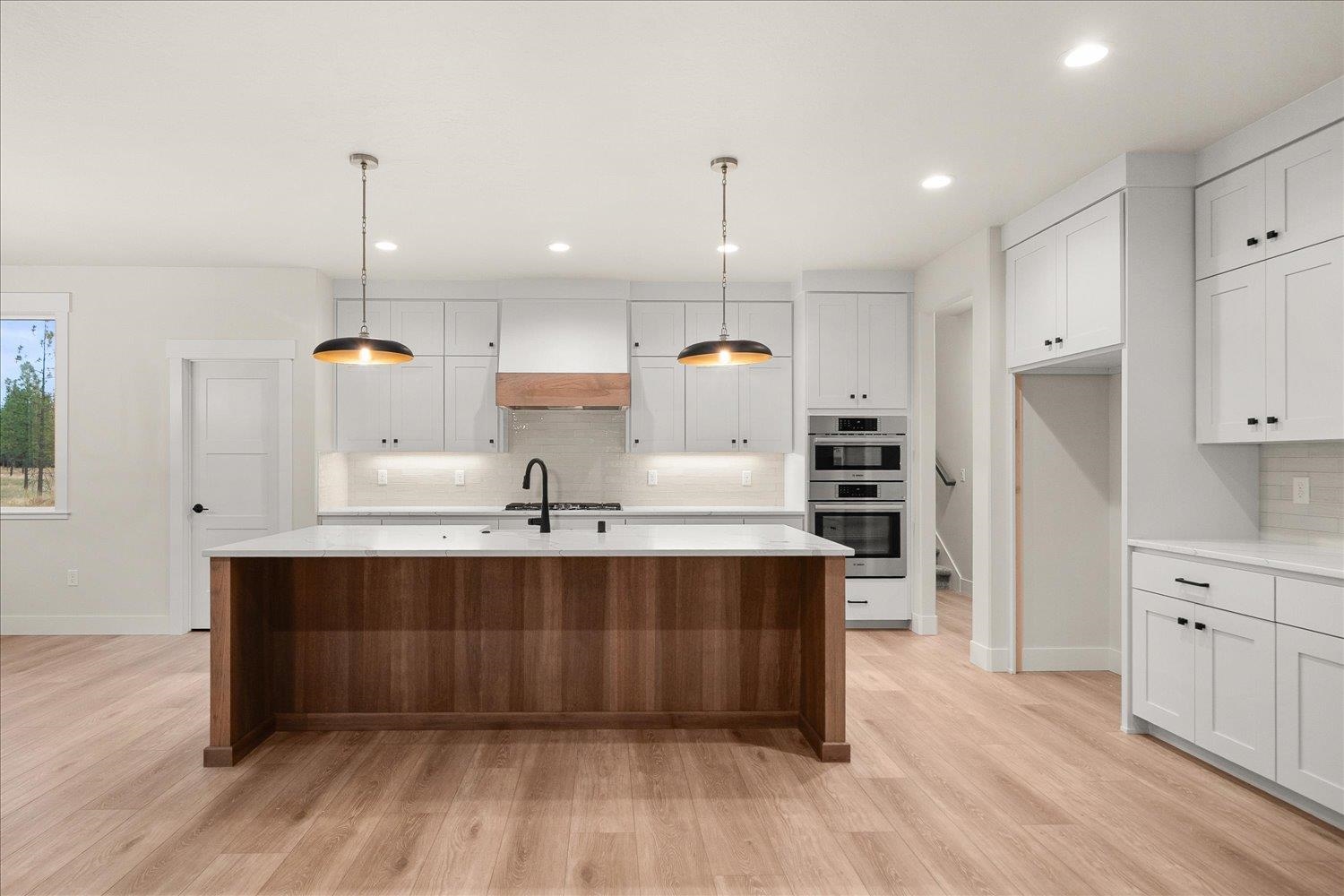 Kitchen with a dark wood island, white shaker cabinets, pendant lights, and built-in double ovens.