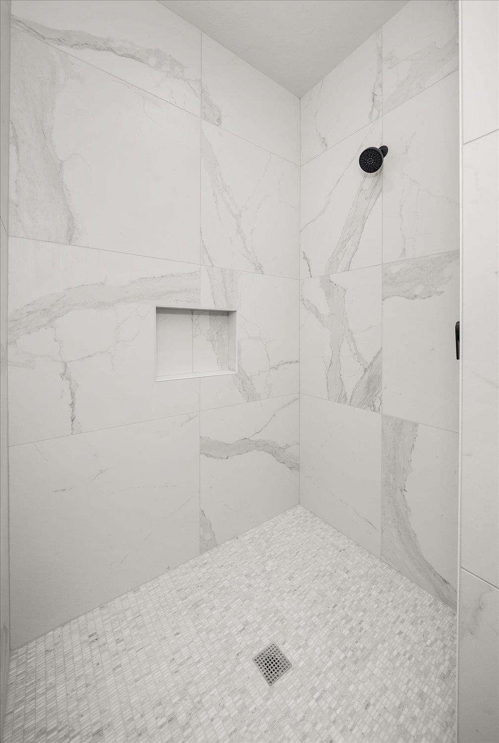 Walk-in shower with marble-look tile, a built-in niche, black showerhead, and mosaic floor.