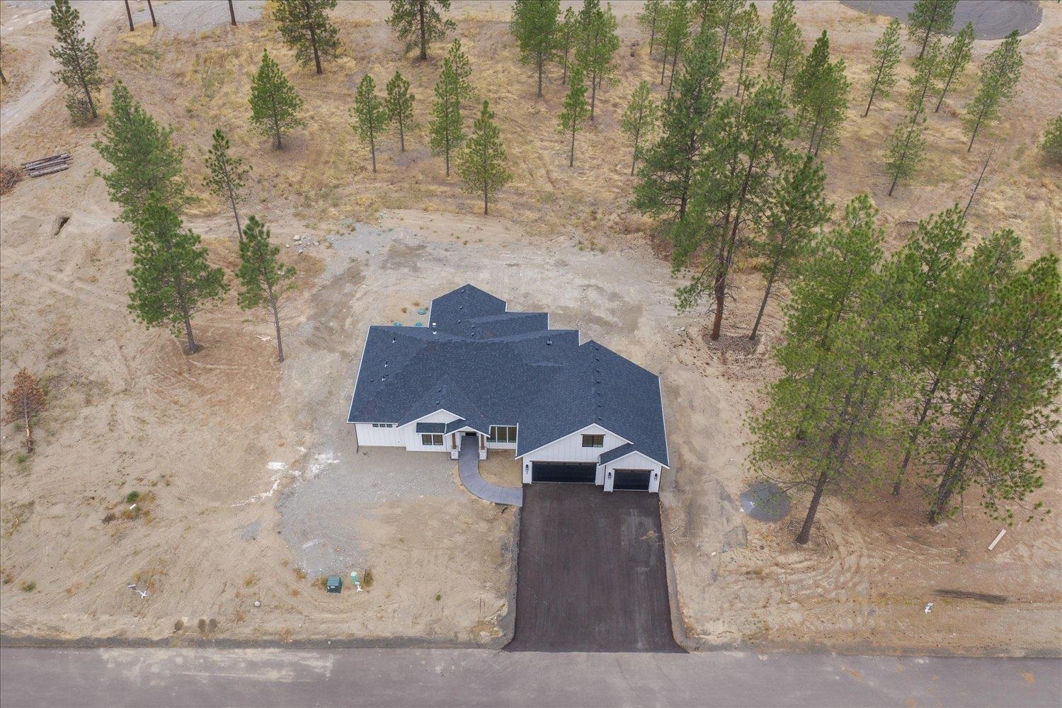 Aerial view of a white home with a dark roof, long driveway, and pine-dotted sandy lot.