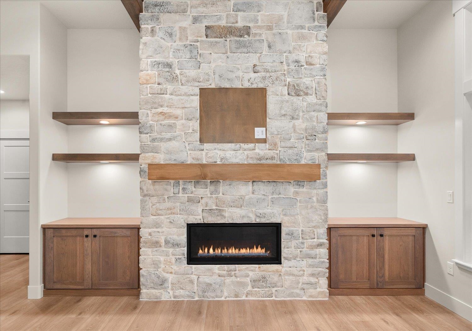 Stone fireplace with a lit gas fire, wood mantel, built-in cabinets, and floating shelves.