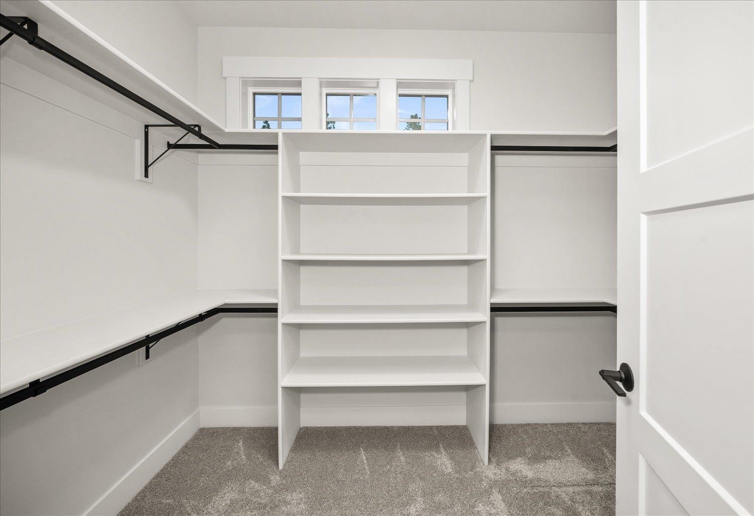 Walk-in closet with built-in white shelving, black hanging rods, and three high windows.